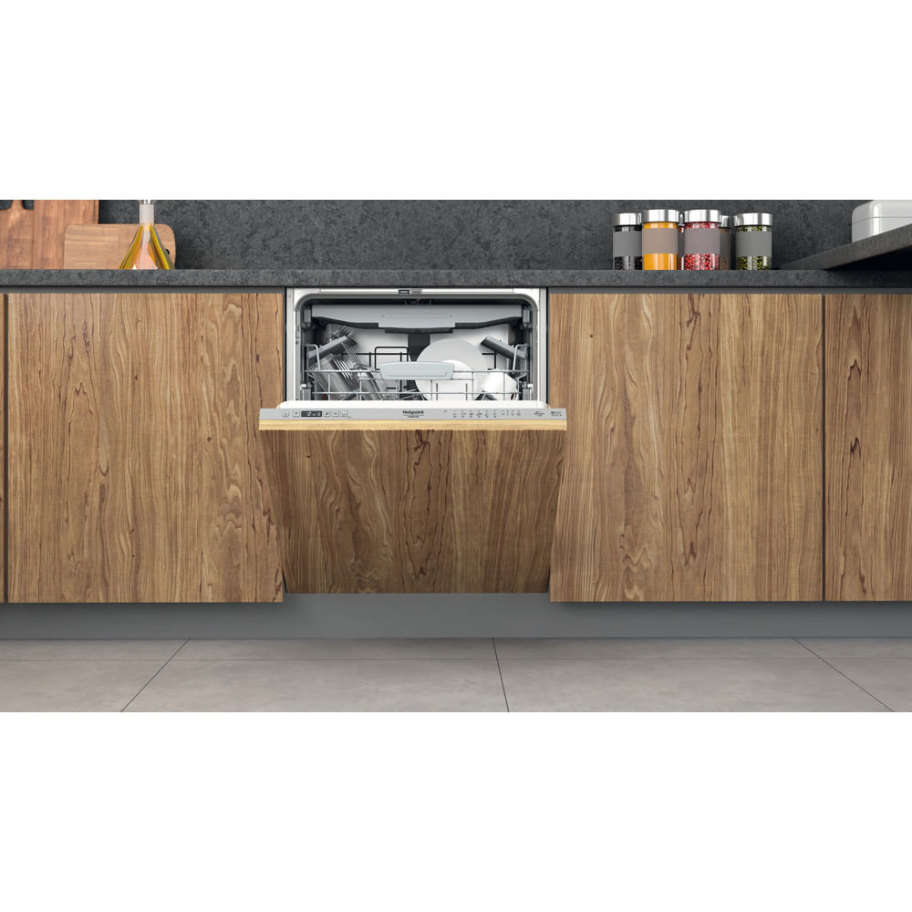 Lavastoviglie aperta in una cucina moderna. Mobili in legno, piano di lavoro grigio e piastrelle. Piatti e posate all'interno.