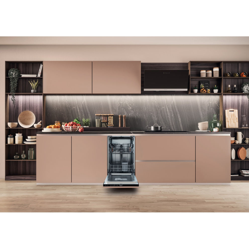 Cucina moderna con lavastoviglie aperta. Armadi color rosa, alzatina in marmo, pavimento in legno e scaffali con stoviglie e decorazioni.