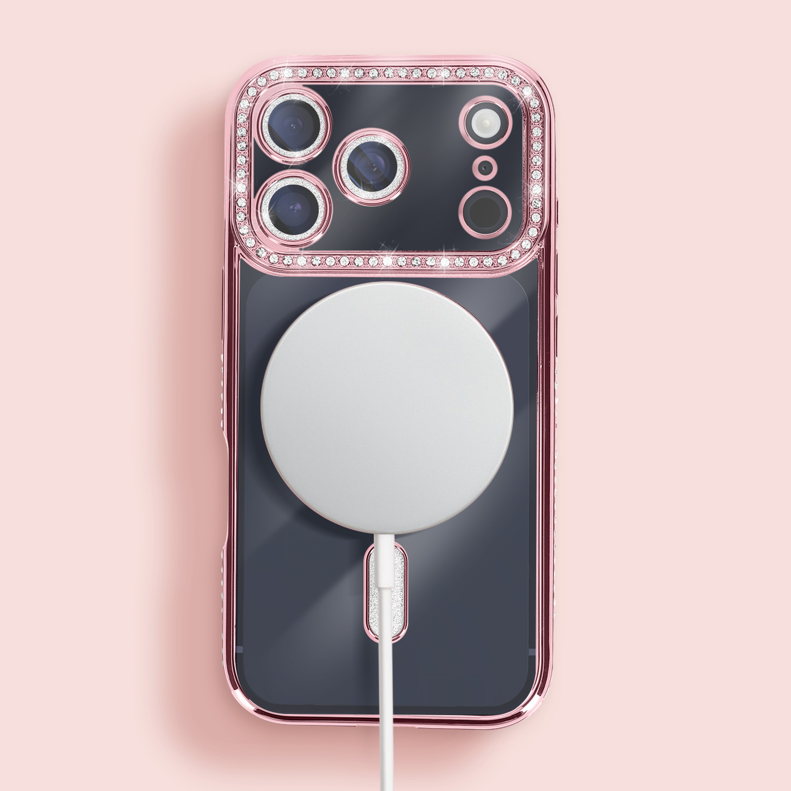 Coque de téléphone rose avec dos transparent, bords ornés de bijoux et chargeur MagSafe blanc sur fond rose.