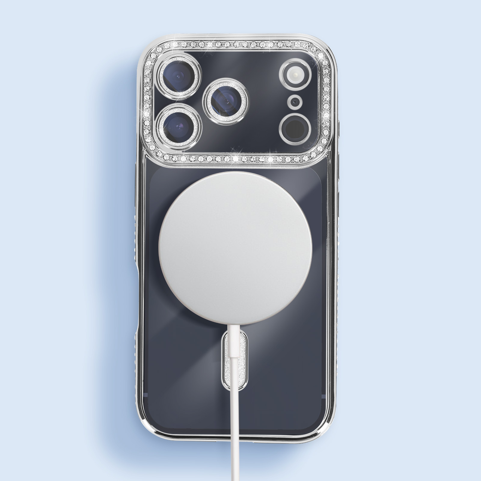 Telefoon in een transparante hoes met zilveren rand, kristallen en een witte cirkelvormige oplader. Lichtblauwe achtergrond.