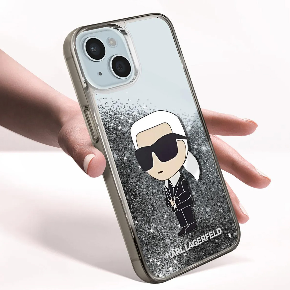 Una custodia per telefono con un design Karl Lagerfeld è tenuta in mano. La custodia presenta uno sfondo glitterato e un cartone animato di Karl.