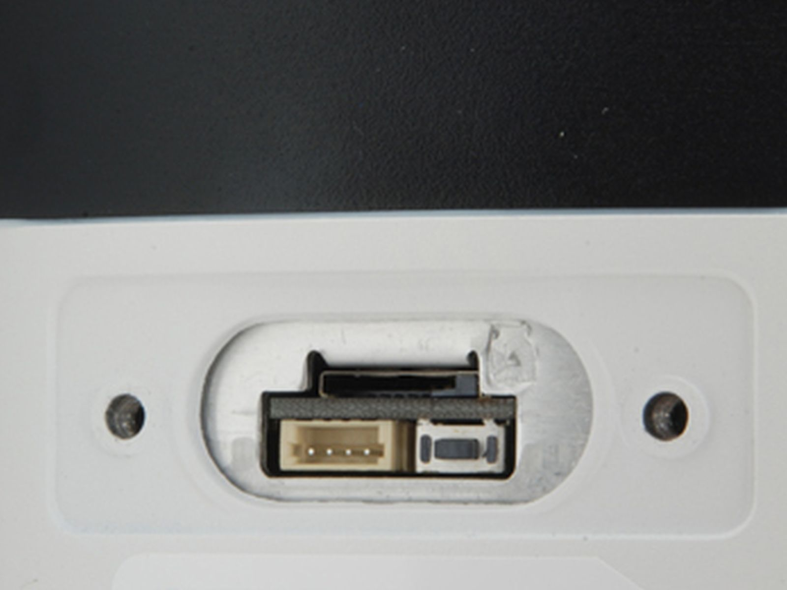 Zbliżenie białego panelu z zagłębionym obszarem zawierającym port USB i inne złącza. Po obu stronach znajdują się dwa otwory.