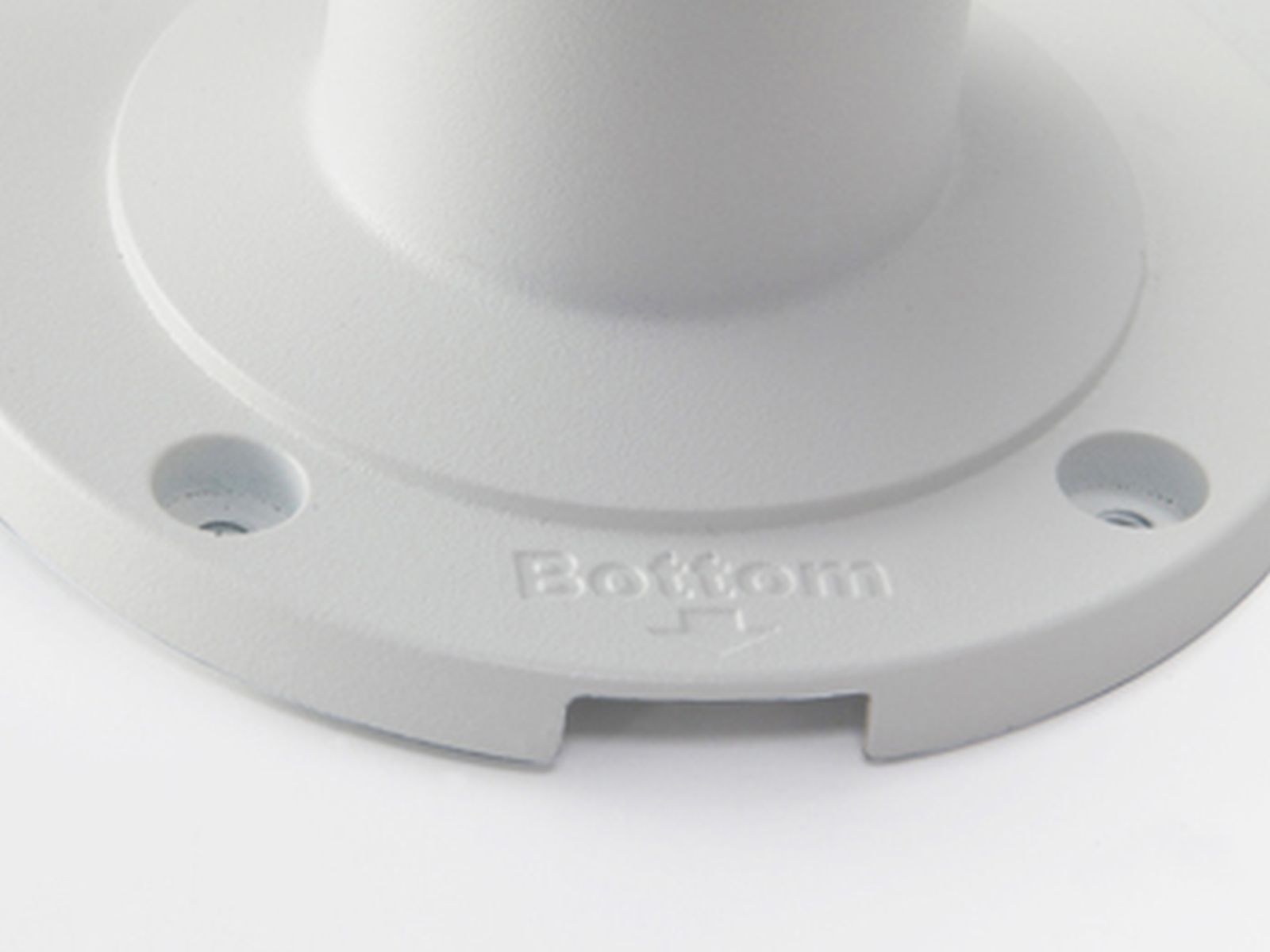 Zbliżenie białej plastikowej podstawy z wytłoczonym słowem 'Bottom'. Widoczne są dwa otwory. Tło jest białe.