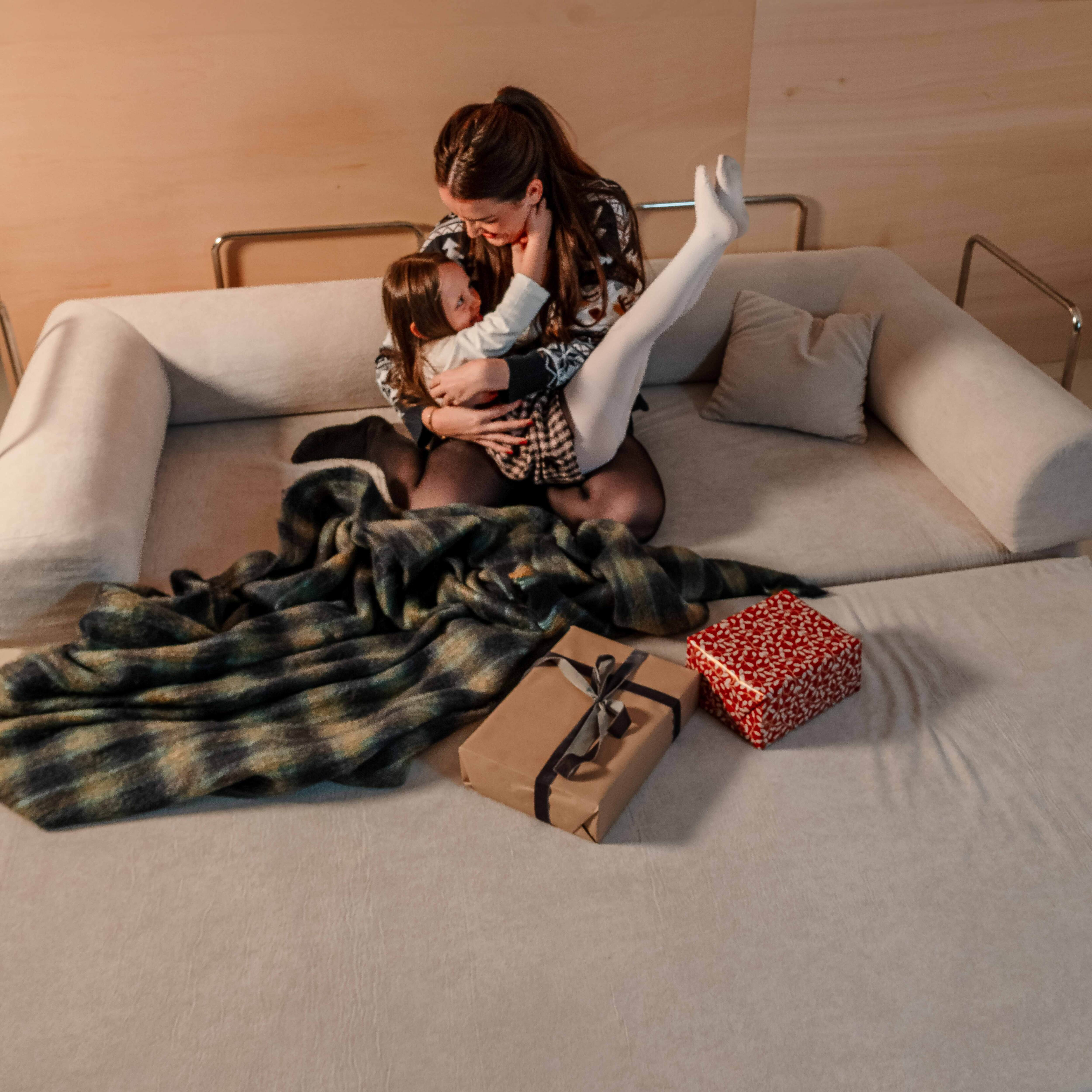 Eine Frau und ein Kind sitzen auf einem Sofa. Auf dem Sofa liegen Geschenke. Auf dem Sofa liegt auch eine Decke.