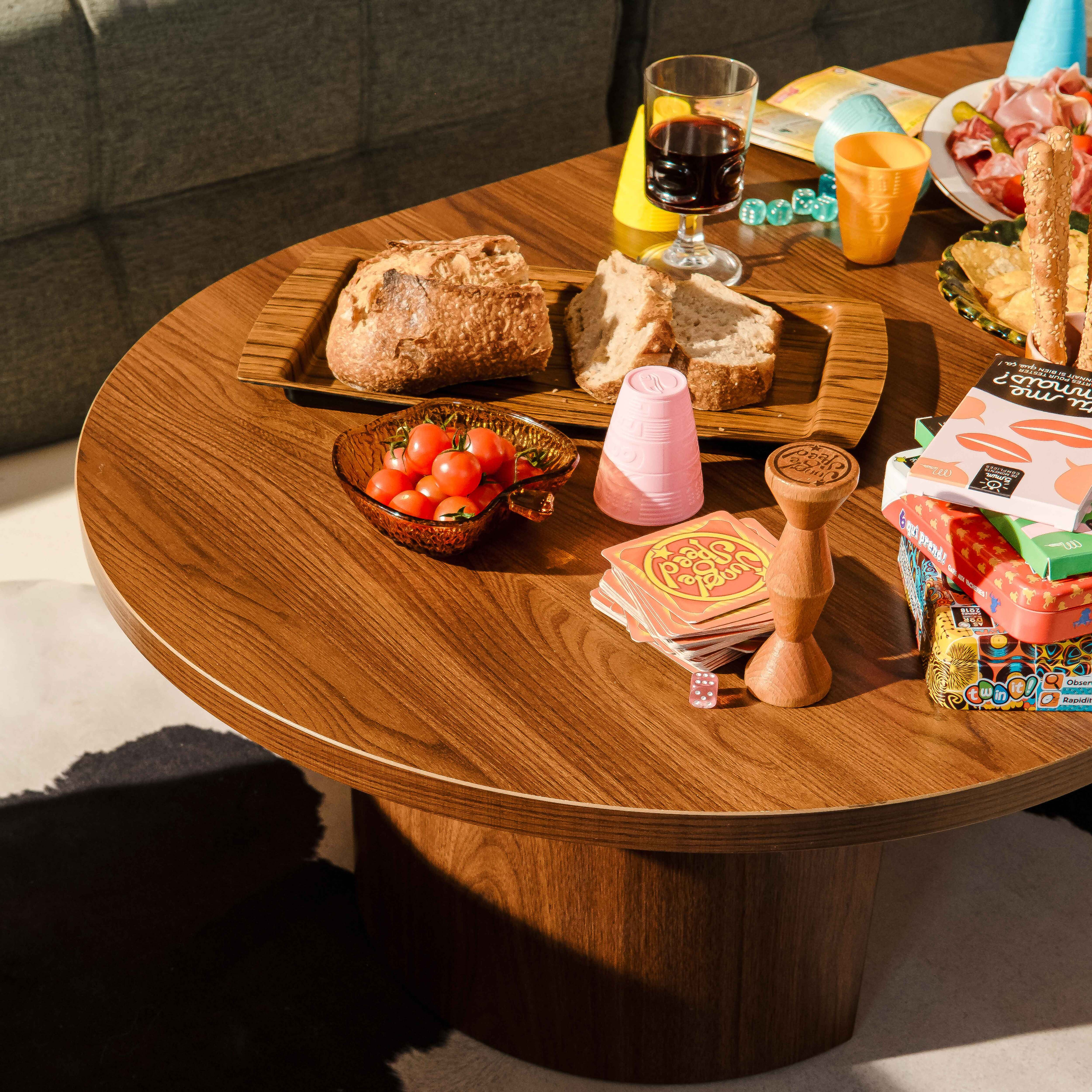 Ein Tisch mit Essen, Getränken und Spielen. Brot, Tomaten, Wein und Brettspiele sind sichtbar.