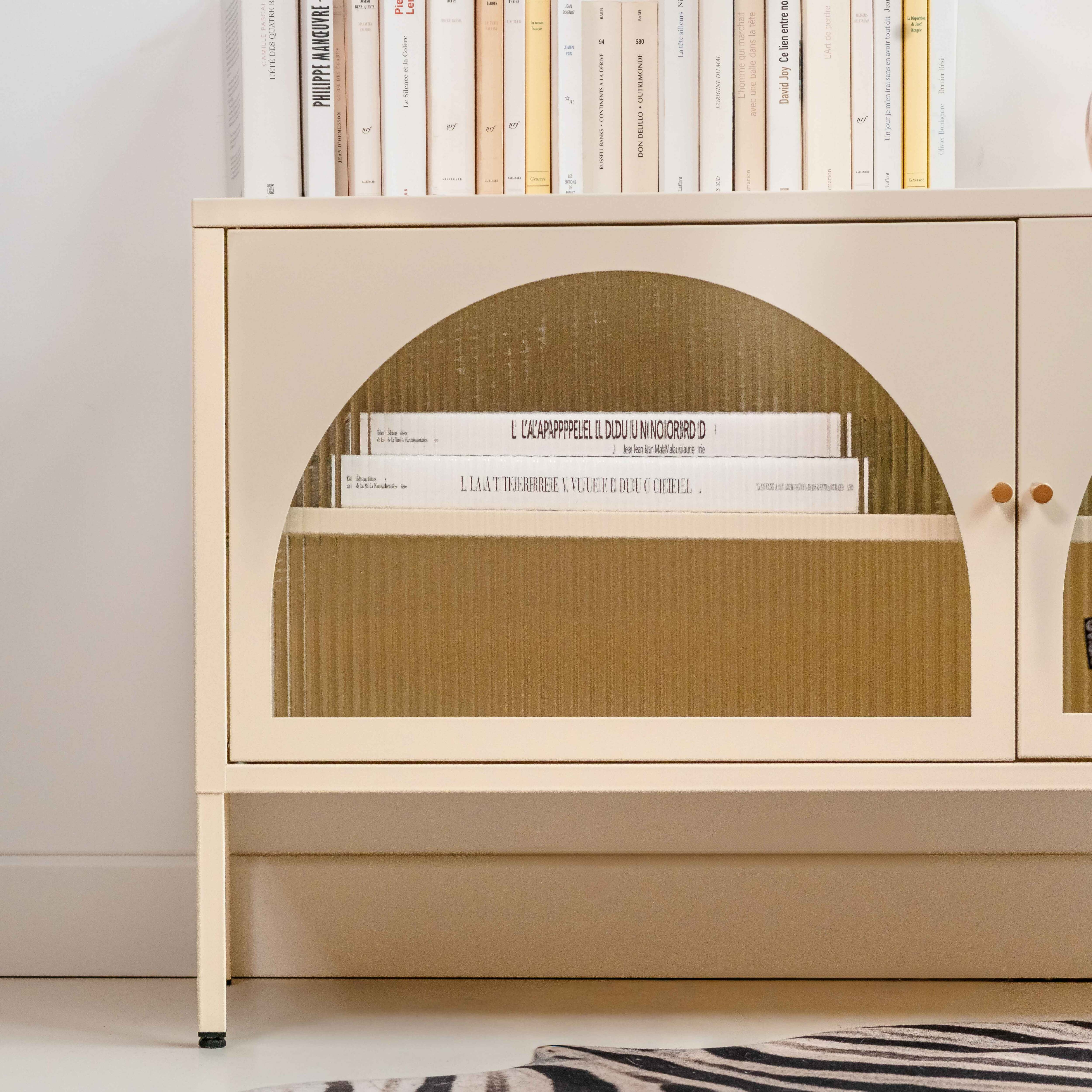 Cremefarbener Schrank mit Büchern, einer gebogenen Glastür und einem Zebrateppich.