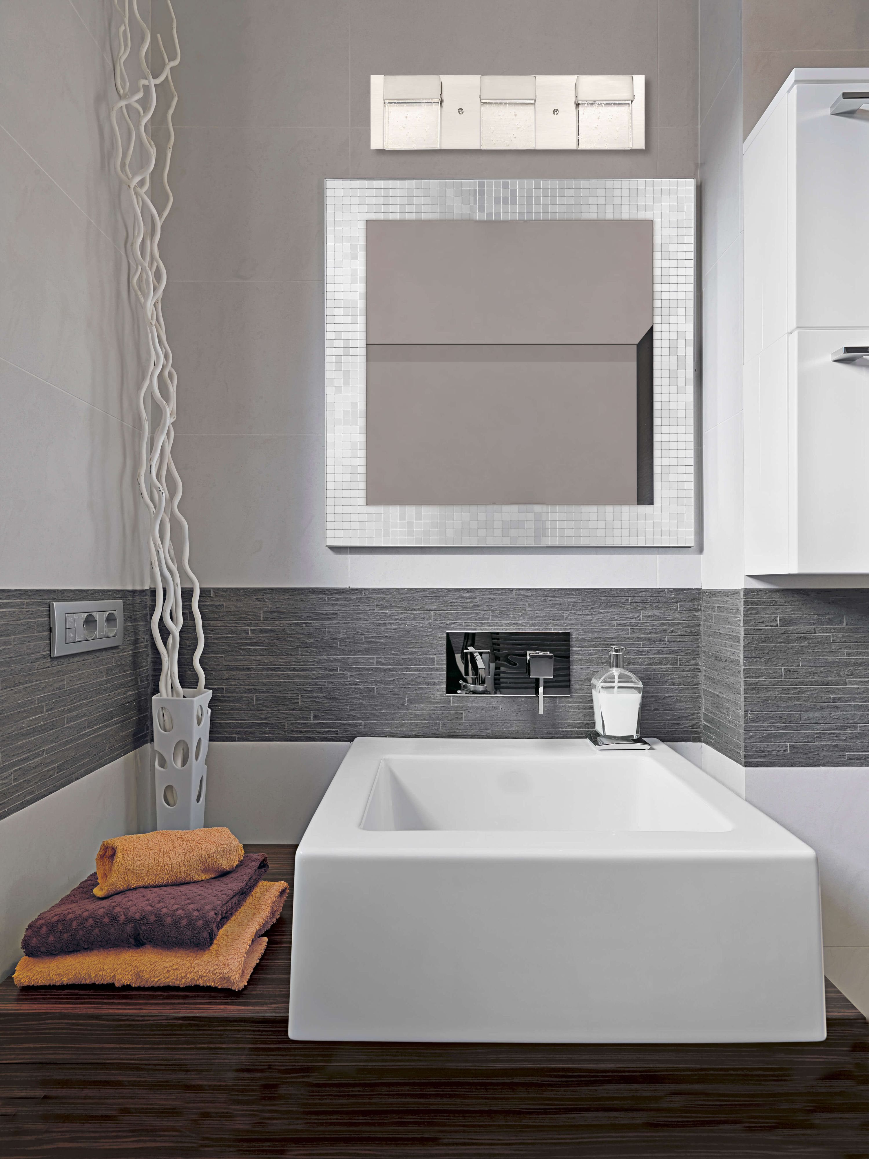 Badezimmer mit quadratischem Waschbecken, Spiegel, Handtüchern und dekorativen Ästen. Grau-weißes Farbschema.