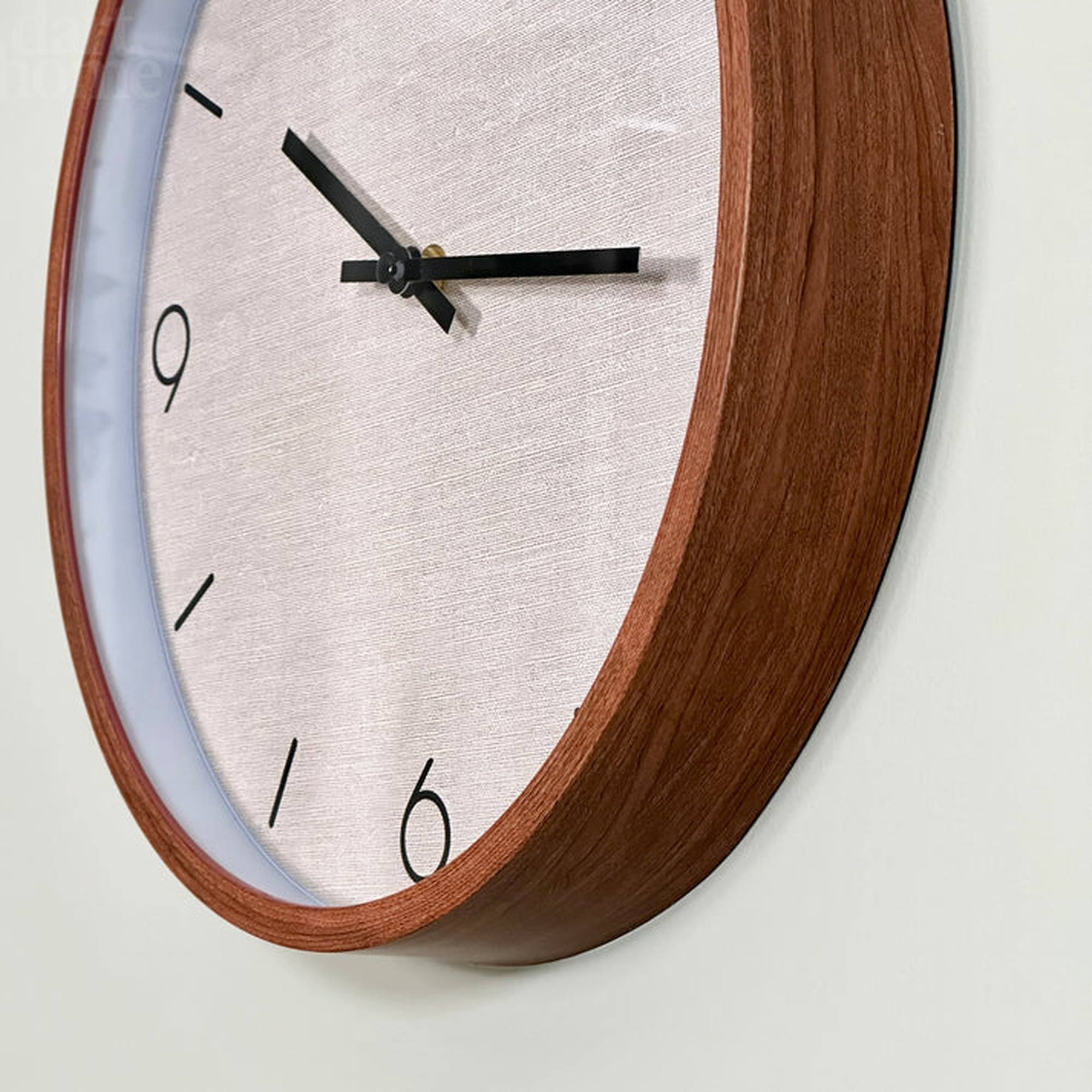 Primer plano de un reloj de madera con manecillas y números negros. El fondo es una pared blanca.