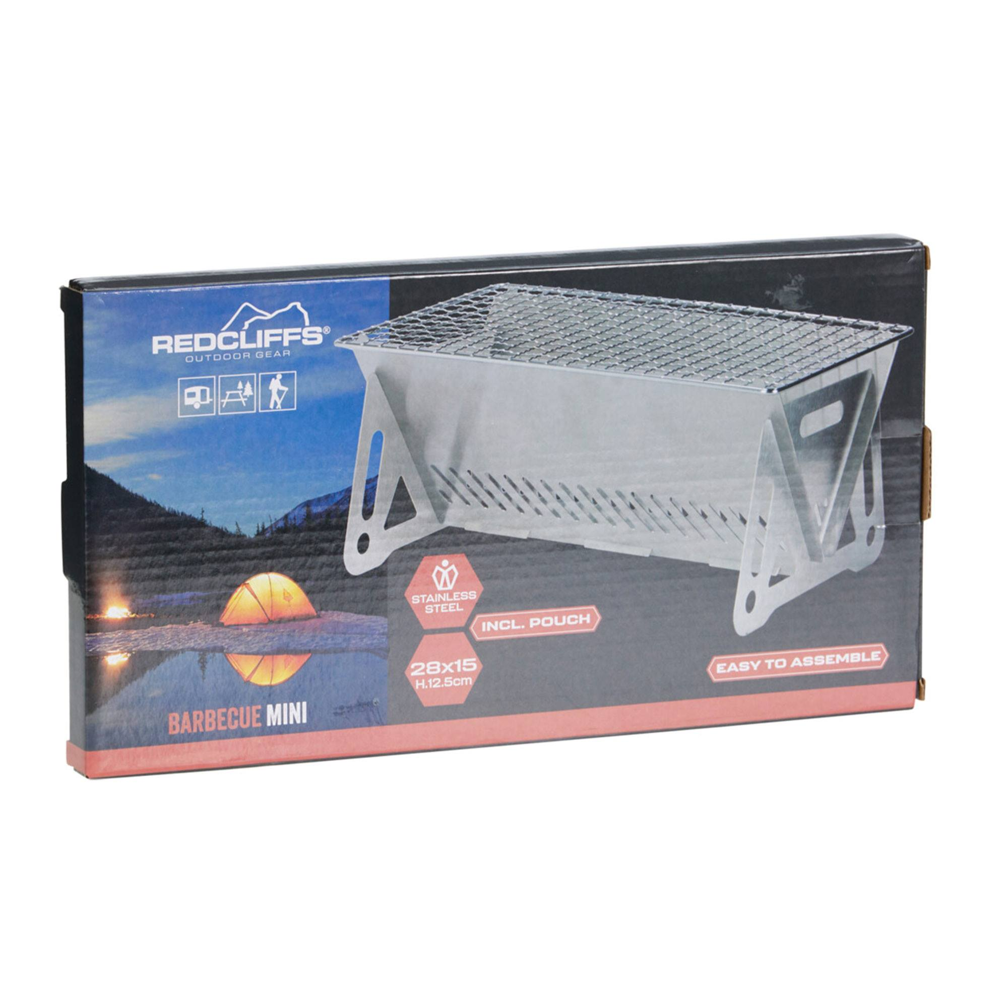 Barbacoa mini Redcliffs en caja. Acero inoxidable, fácil de montar. Incluye una bolsa. La caja muestra una escena de tienda.