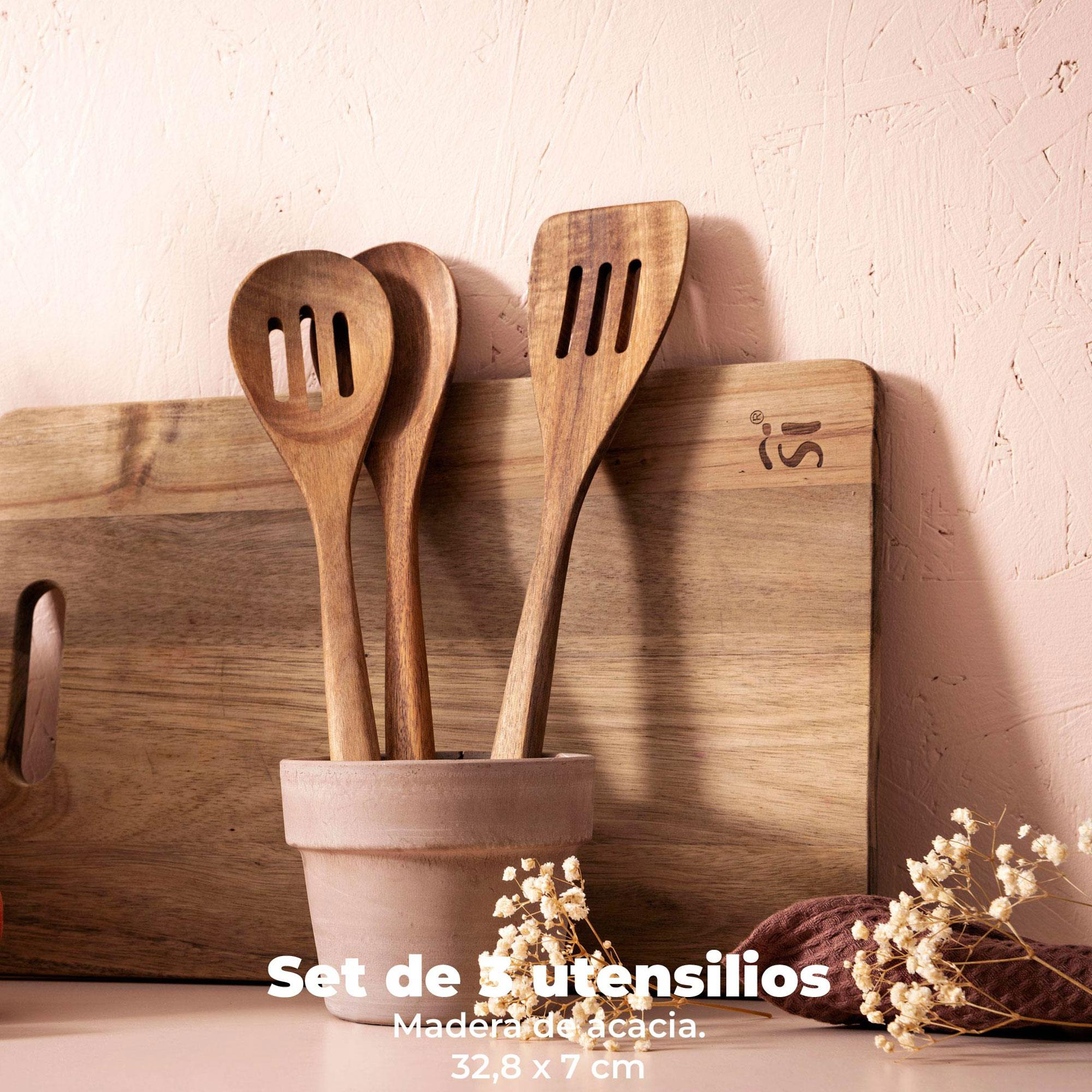 Utensilios de cocina de madera en una maceta, tabla de cortar y flores contra una pared rosa. Texto: Set de 3 utensilios, madera de acacia.