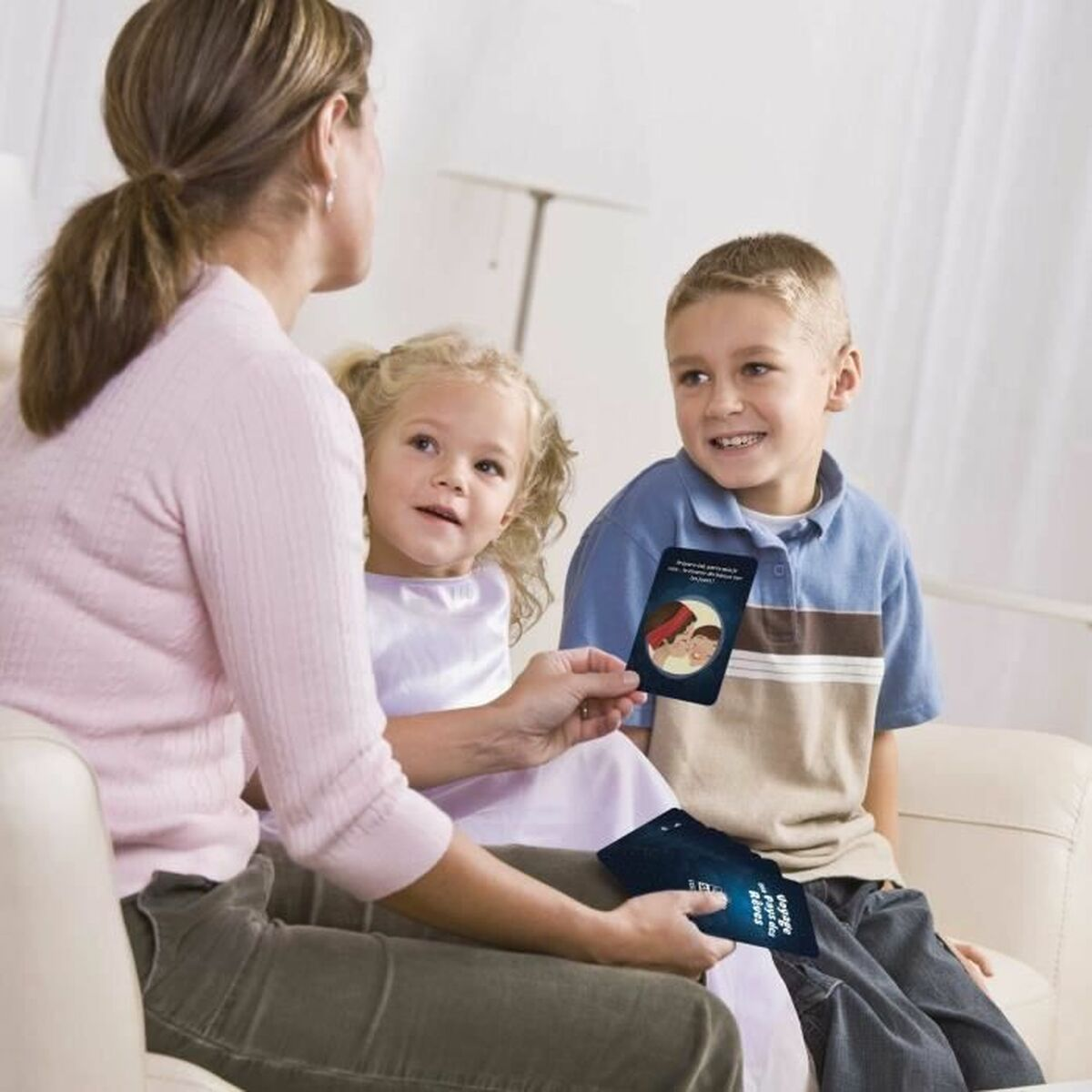 Una donna mostra delle carte a due bambini su un divano. I bambini guardano le carte con interesse. Una carta mostra due persone.