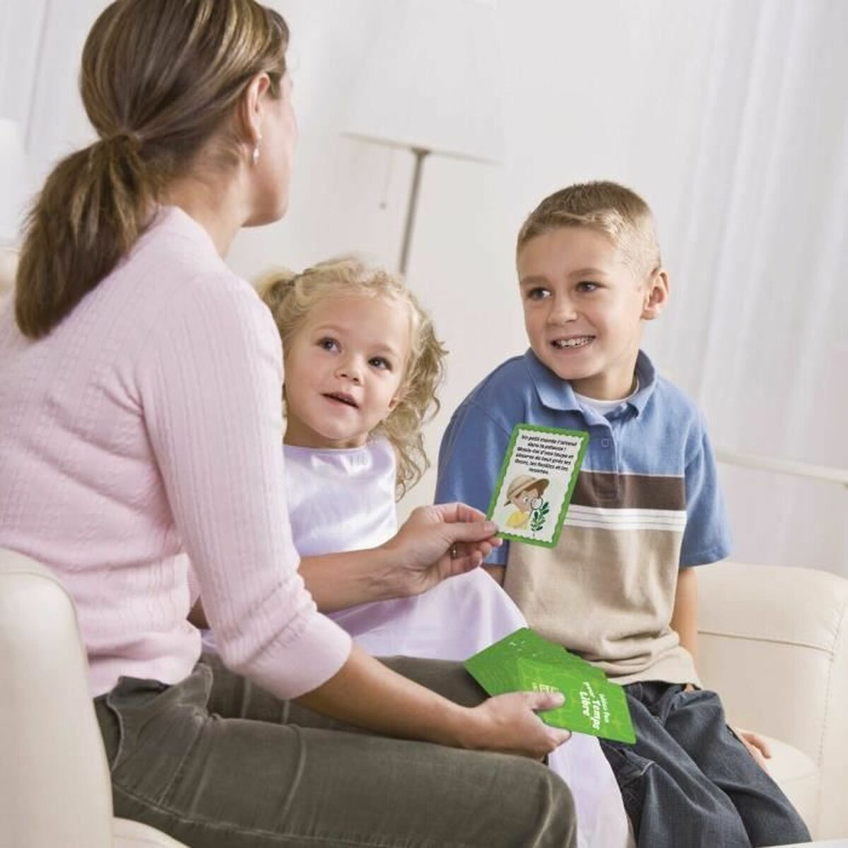 Una donna mostra delle carte a due bambini. I bambini guardano in alto, sorridendo. Le carte sono verdi con testo e immagini.