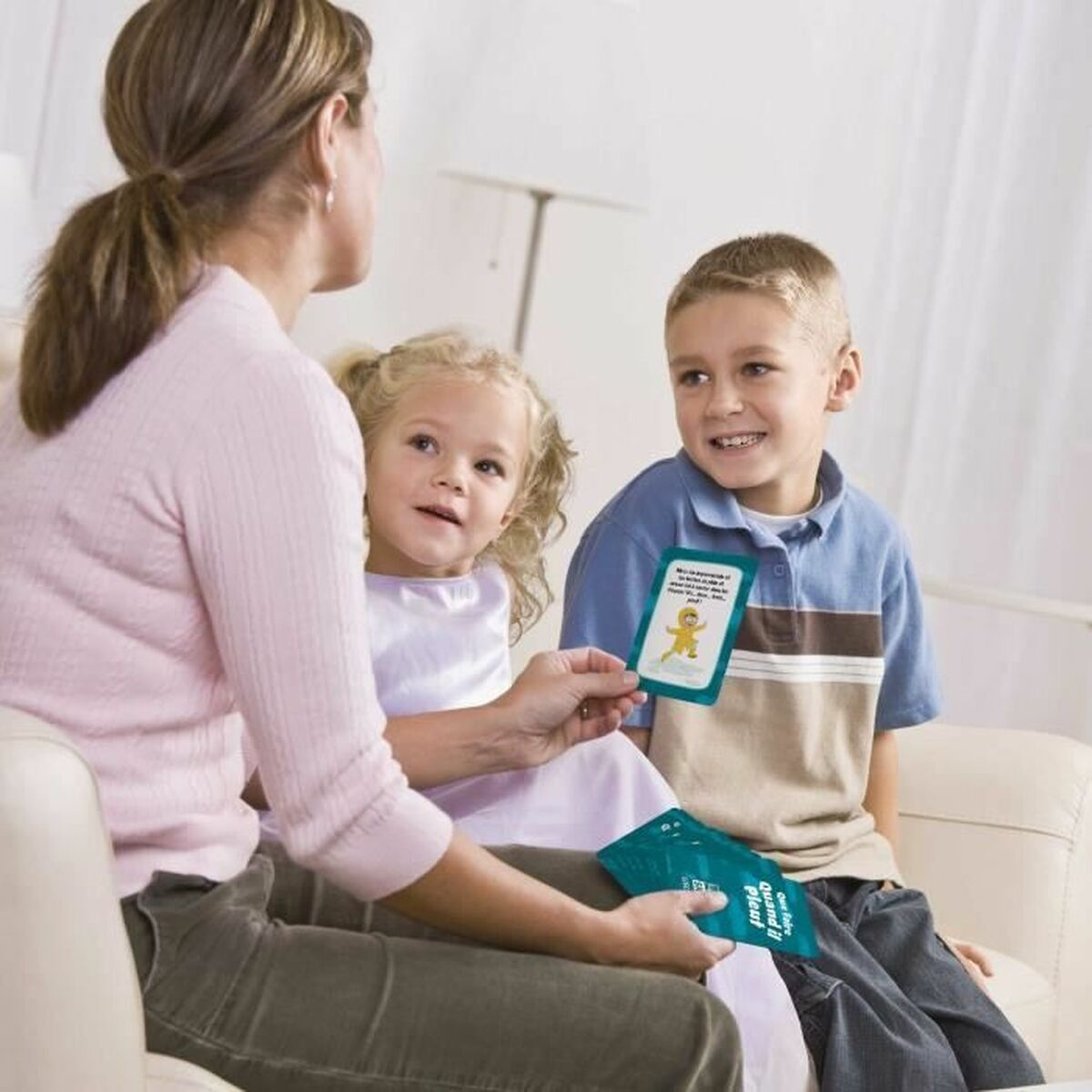 Una donna mostra delle carte a due bambini. Il ragazzo sorride, mentre la bambina e la donna guardano le carte. Sono seduti su un divano bianco.