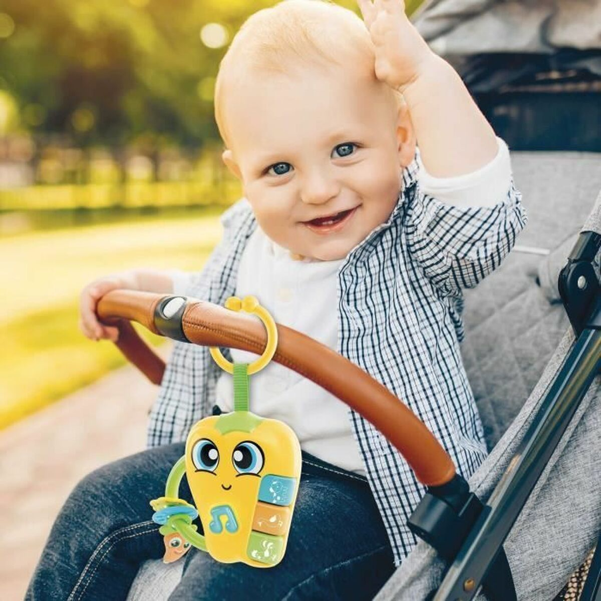 Un bambino sorridente in un passeggino alza la mano. Un giocattolo giallo è appeso al manico.