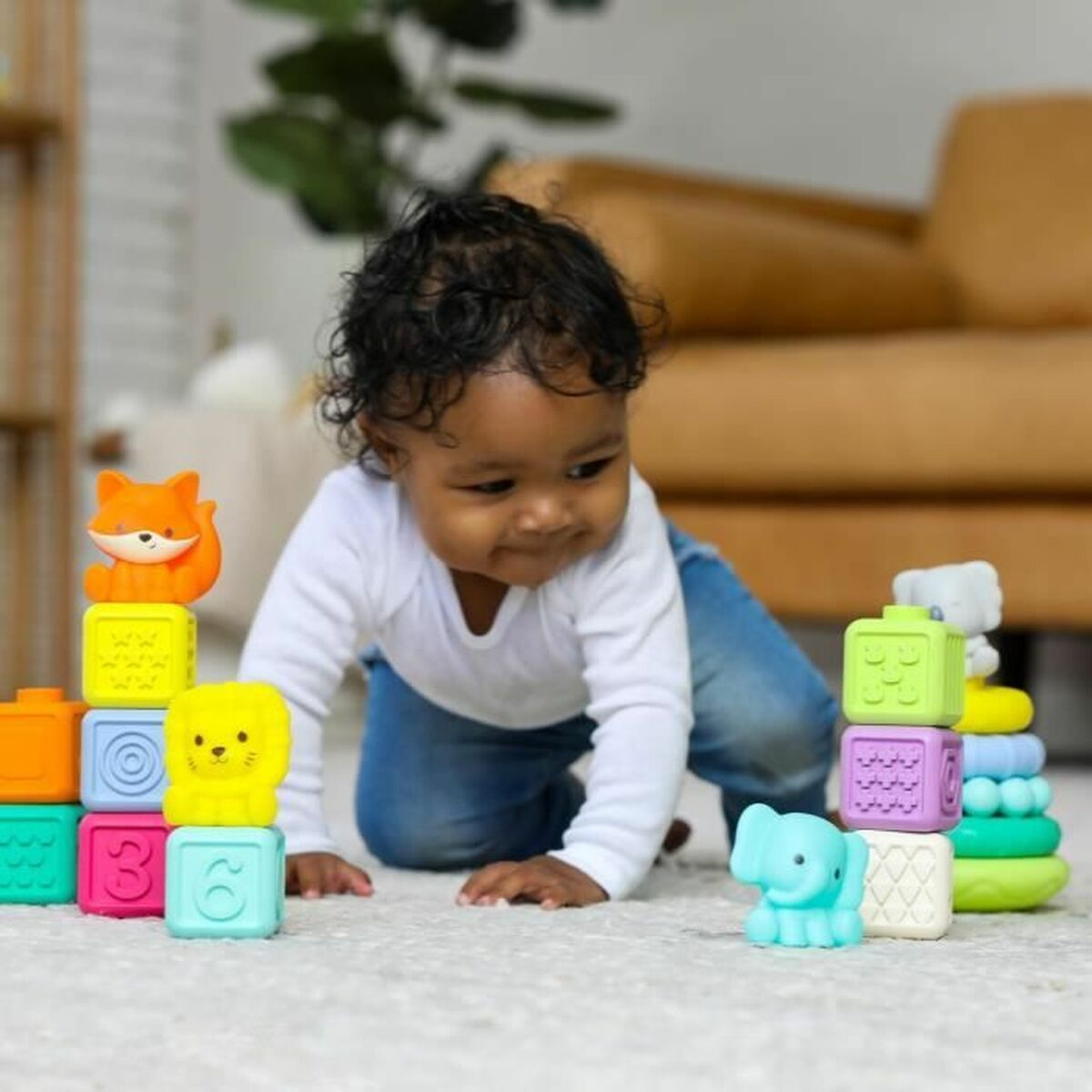 Un bébé joue avec des blocs colorés et des jouets animaux sur un tapis blanc. Un canapé est en arrière-plan.