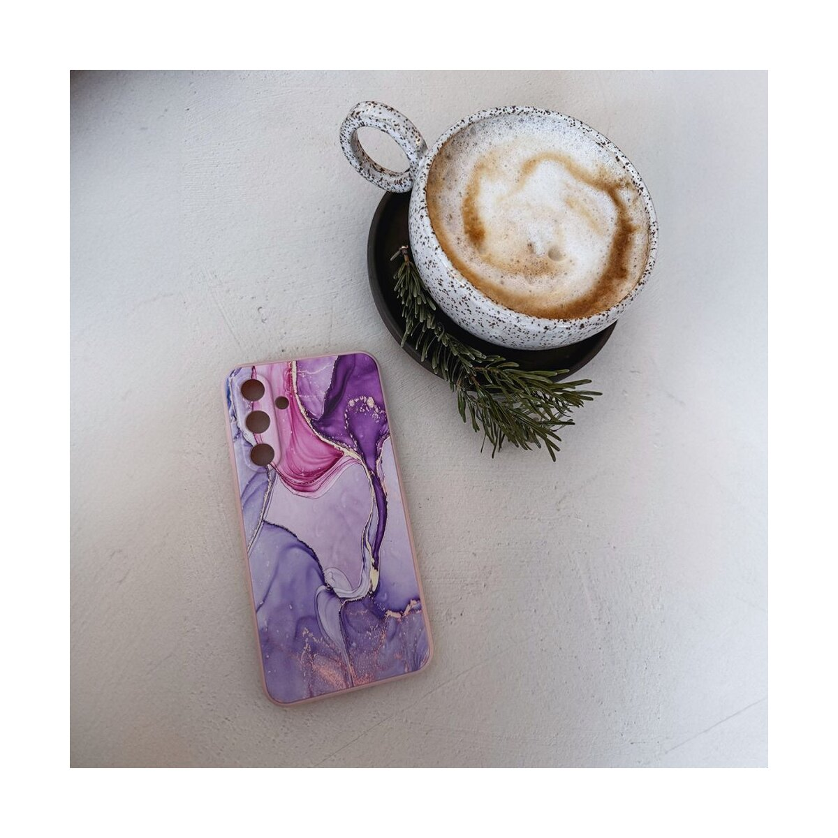 Ein Handycase mit lila und rosa Marmordesign, eine Tasse Kaffee und ein Zweig Rosmarin auf weißem Untergrund.