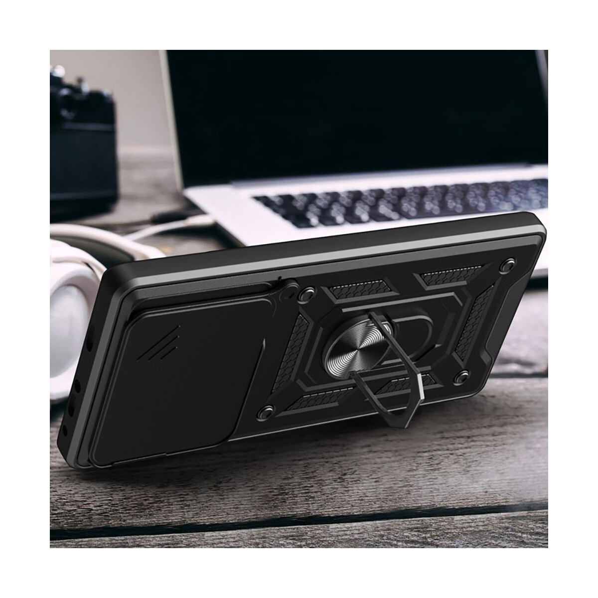 Schwarze Handyhülle mit Ringhalter auf einem Holztisch. Ein Laptop und Kopfhörer sind im Hintergrund.