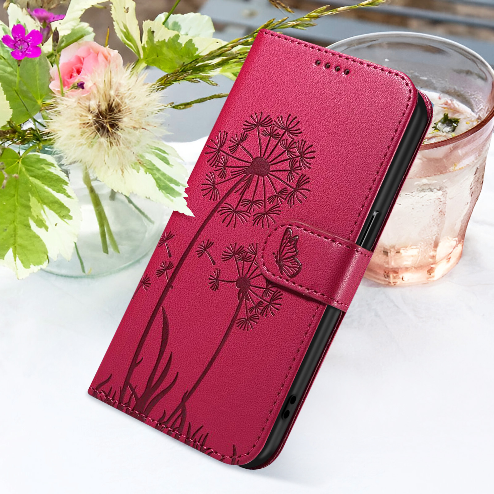 Una custodia rossa per telefono con disegni di dente di leone e farfalla, accanto a un bicchiere d'acqua e fiori.