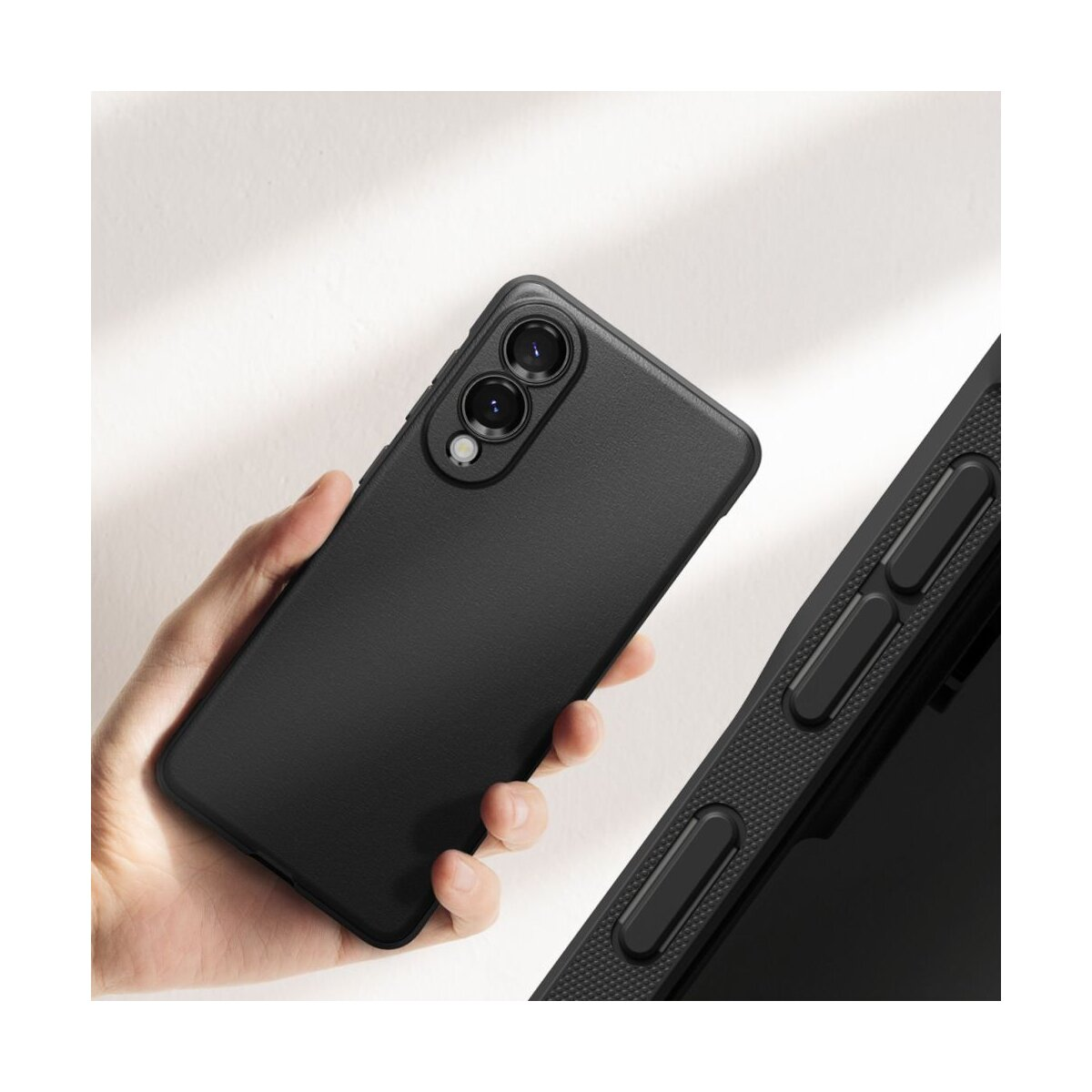 Eine Hand, die ein schwarzes Telefon mit Doppelkamera hält. Ein weiterer schwarzer Telefonteil mit Tasten befindet sich rechts auf weißem Hintergrund.