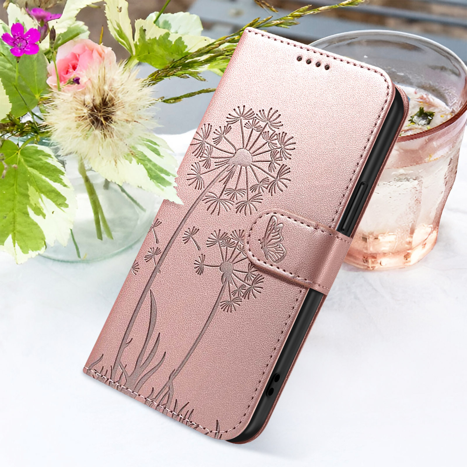 Eine roségoldene Handyhülle mit Pusteblumen-Design liegt in der Nähe eines Wasserglases und Blumen.