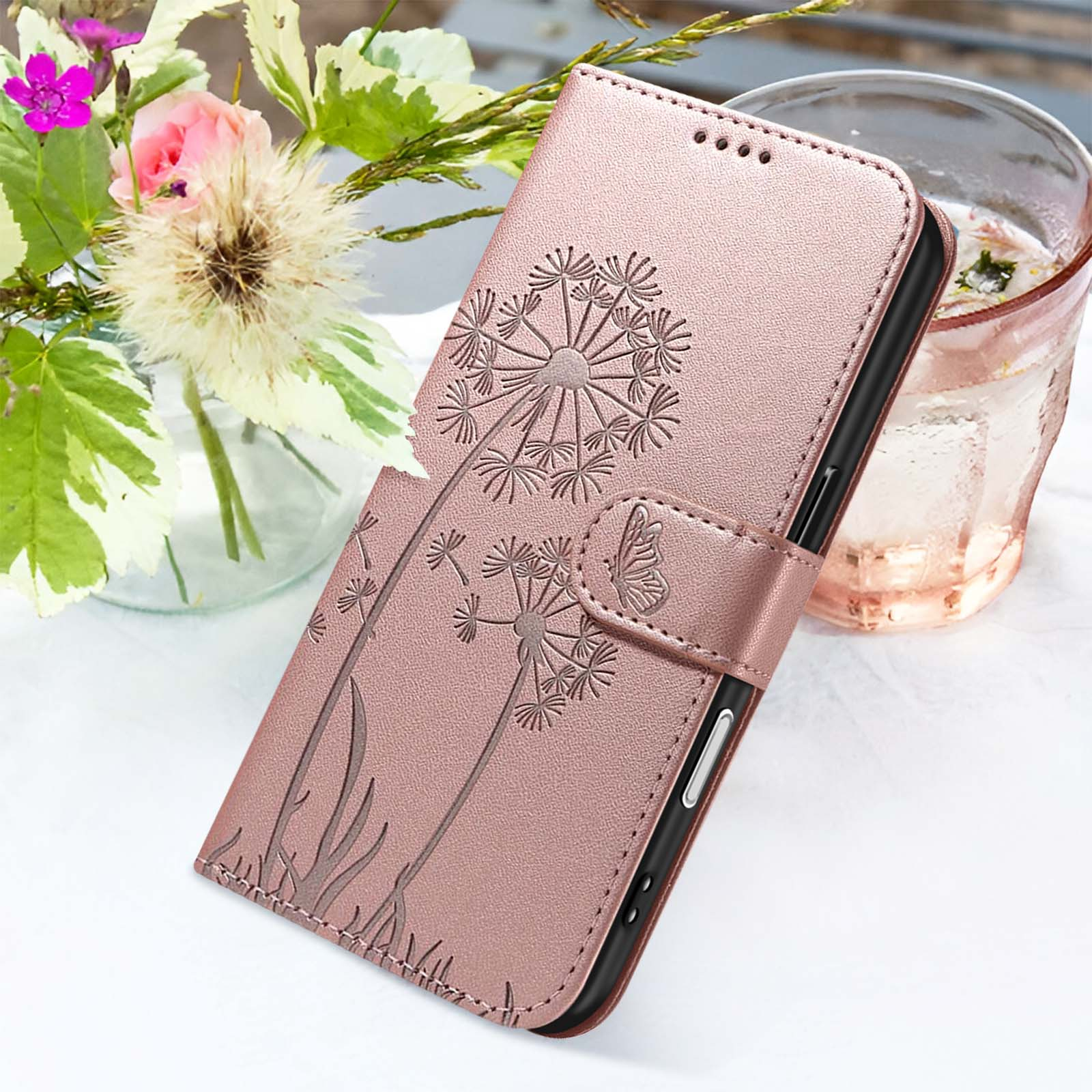 Custodia rosa per telefono con design di dente di leone, accanto a un bicchiere d'acqua e fiori.