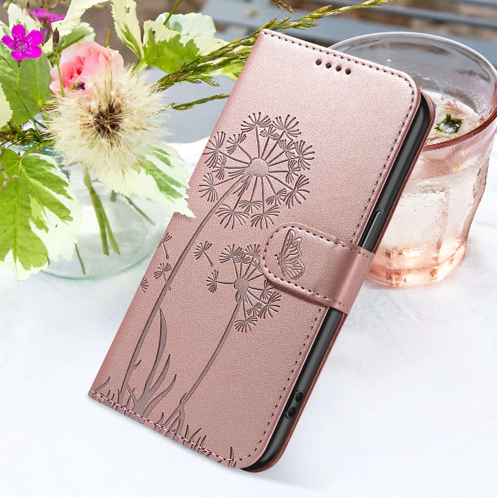 Una custodia per telefono rosa con design a dente di leone, accanto a fiori e un bicchiere d'acqua.