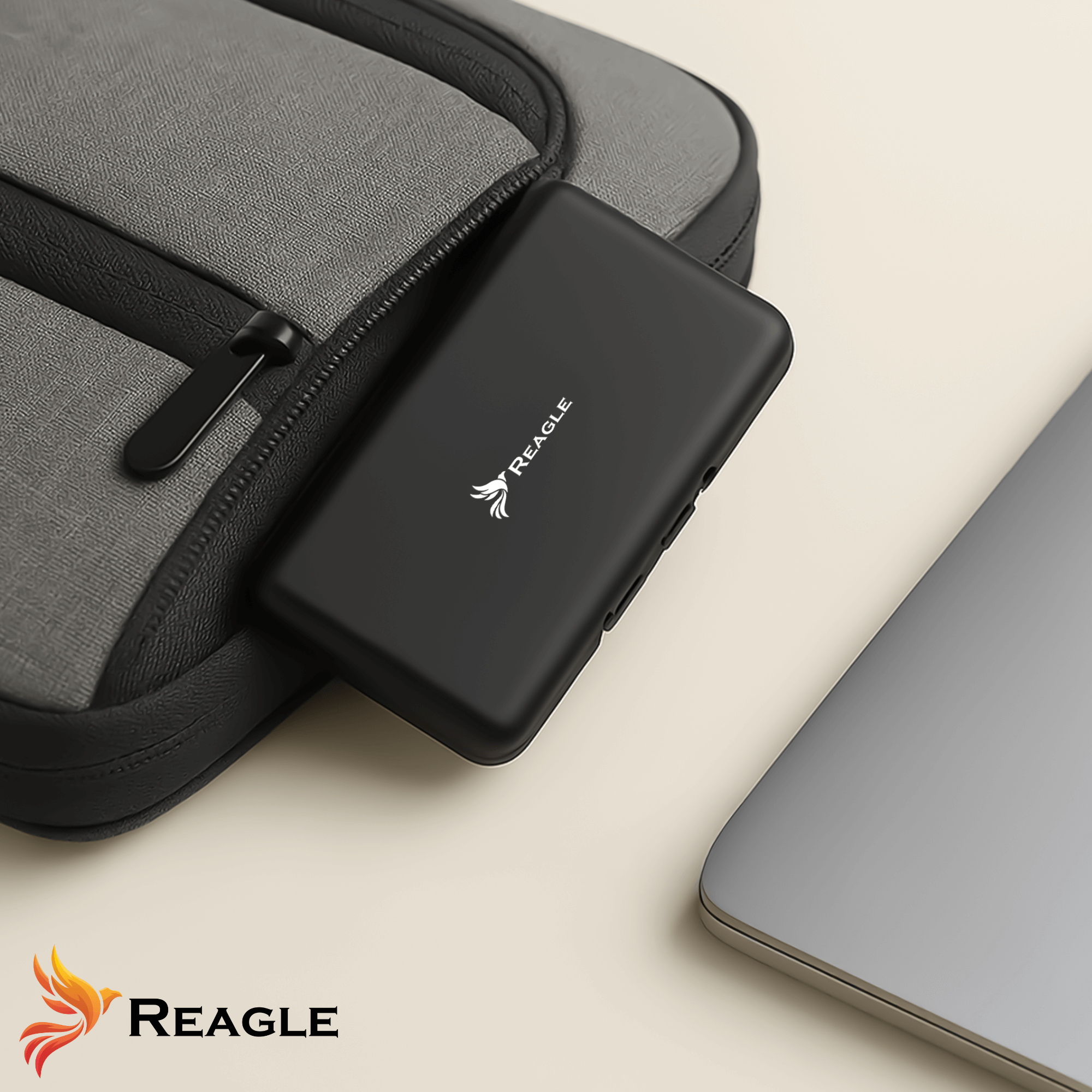 Dispositivo Reagle nero in una borsa grigia e un laptop argentato su una superficie crema.