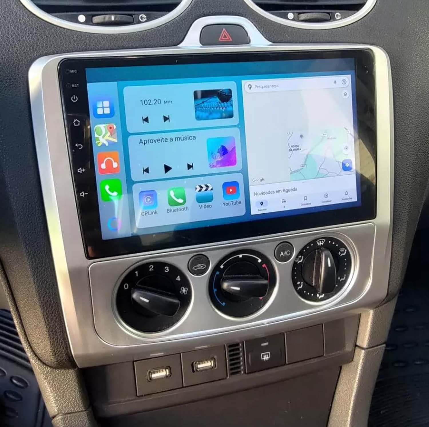 Cruscotto dell'auto con display touchscreen con controlli musicali e navigazione. Sotto, comandi climatici e porte USB.
