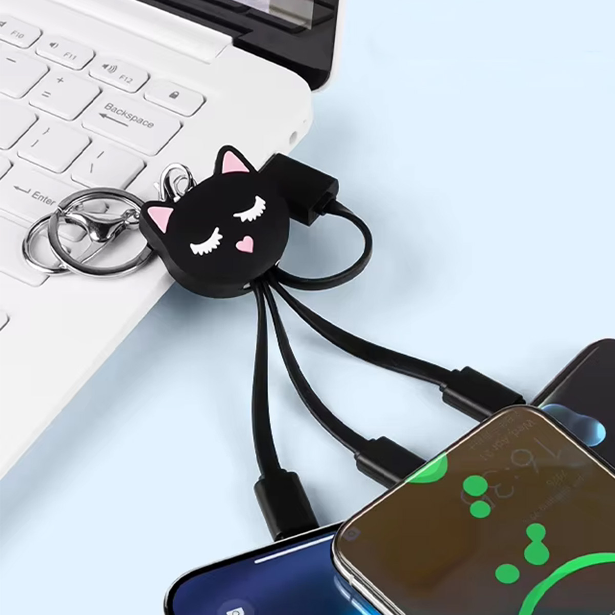 Un caricabatterie USB a forma di gatto nero collegato a un laptop e a tre smartphone. Il gatto ha accenti rosa. I telefoni mostrano schermate di ricarica.