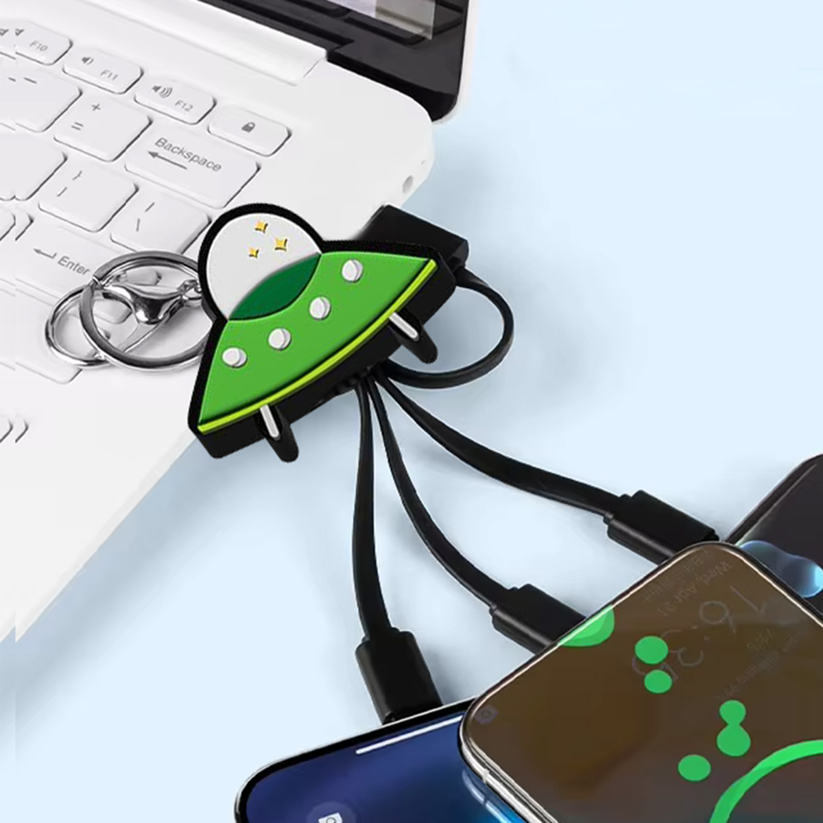 Un caricatore USB a forma di alieno collegato a un laptop e a tre telefoni. L'alieno è verde e bianco. I telefoni sono neri.