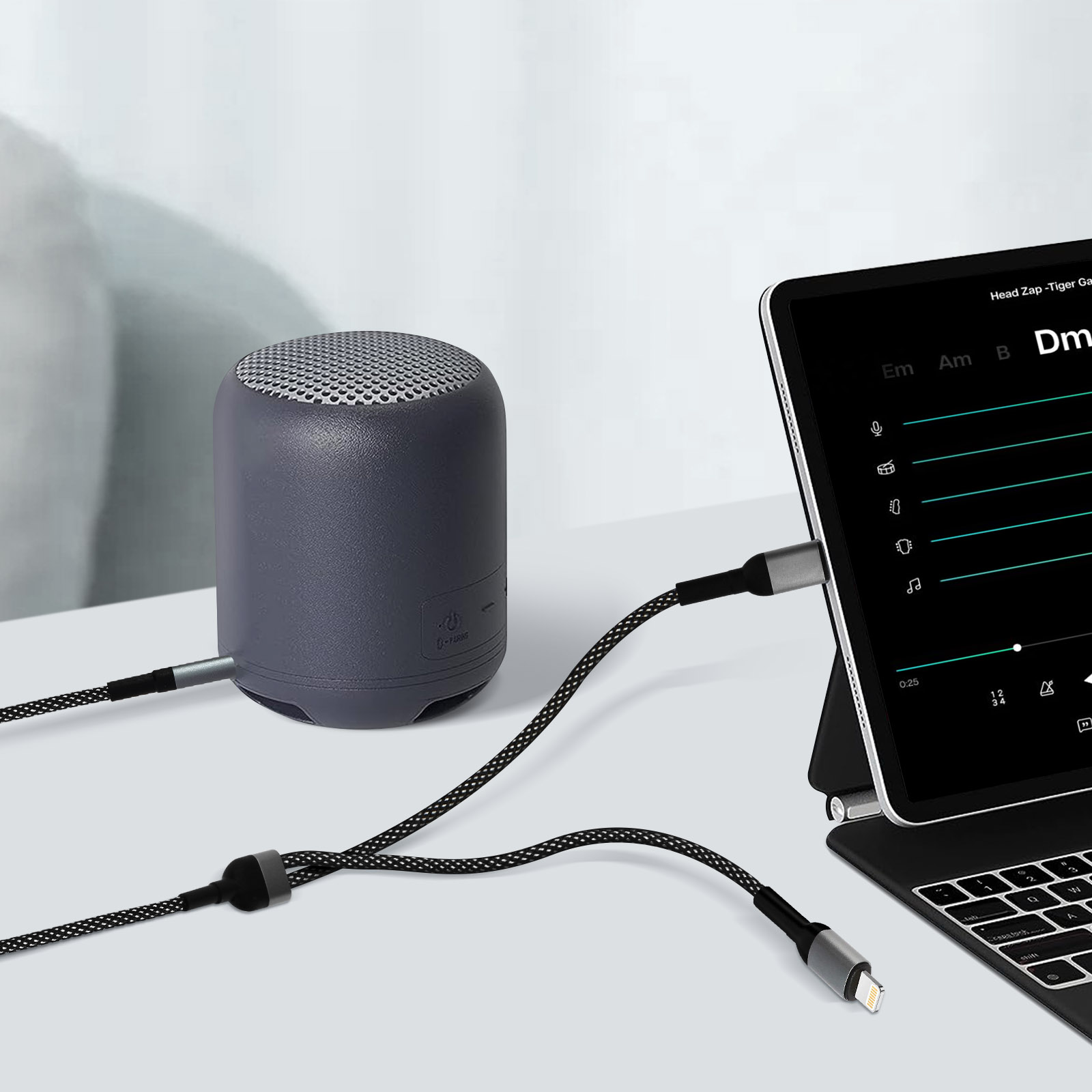Un altoparlante grigio con un tablet collegato tramite cavo, che mostra un'app musicale. La tastiera è nera.