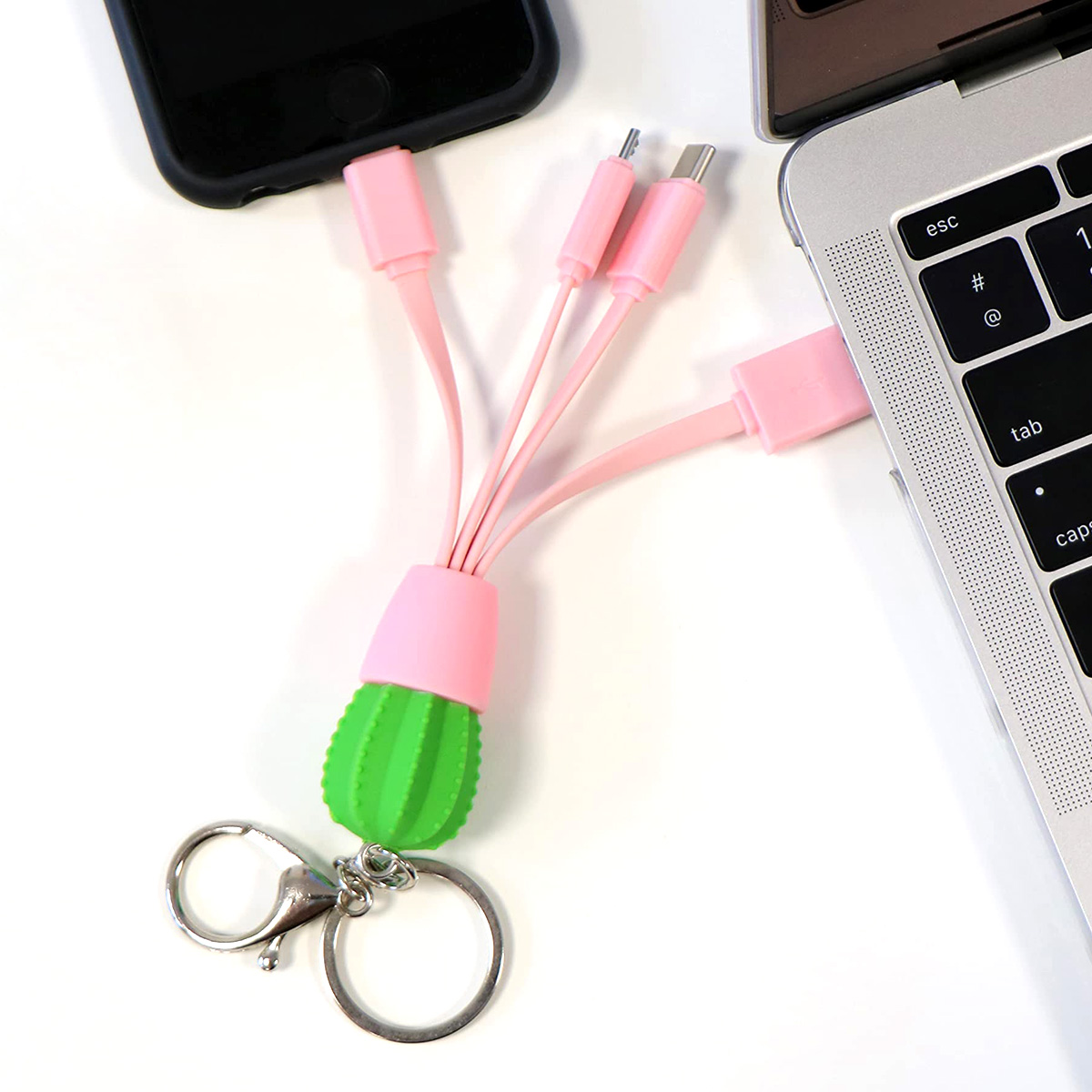 Un caricabatterie USB a forma di cactus rosa e verde con più connettori, attaccato a un portachiavi, collegato a laptop e telefono.