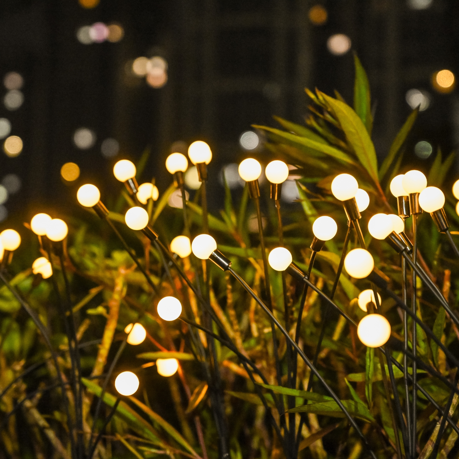 Primo piano di luci decorative in un giardino. Lampadine rotonde e luminose su sottili steli neri tra il fogliame verde.