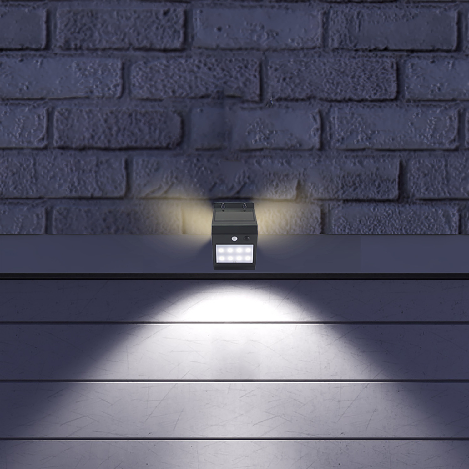 Una luce solare nera è montata su una superficie, contro un muro di mattoni. La luce illumina la superficie sottostante e il muro.