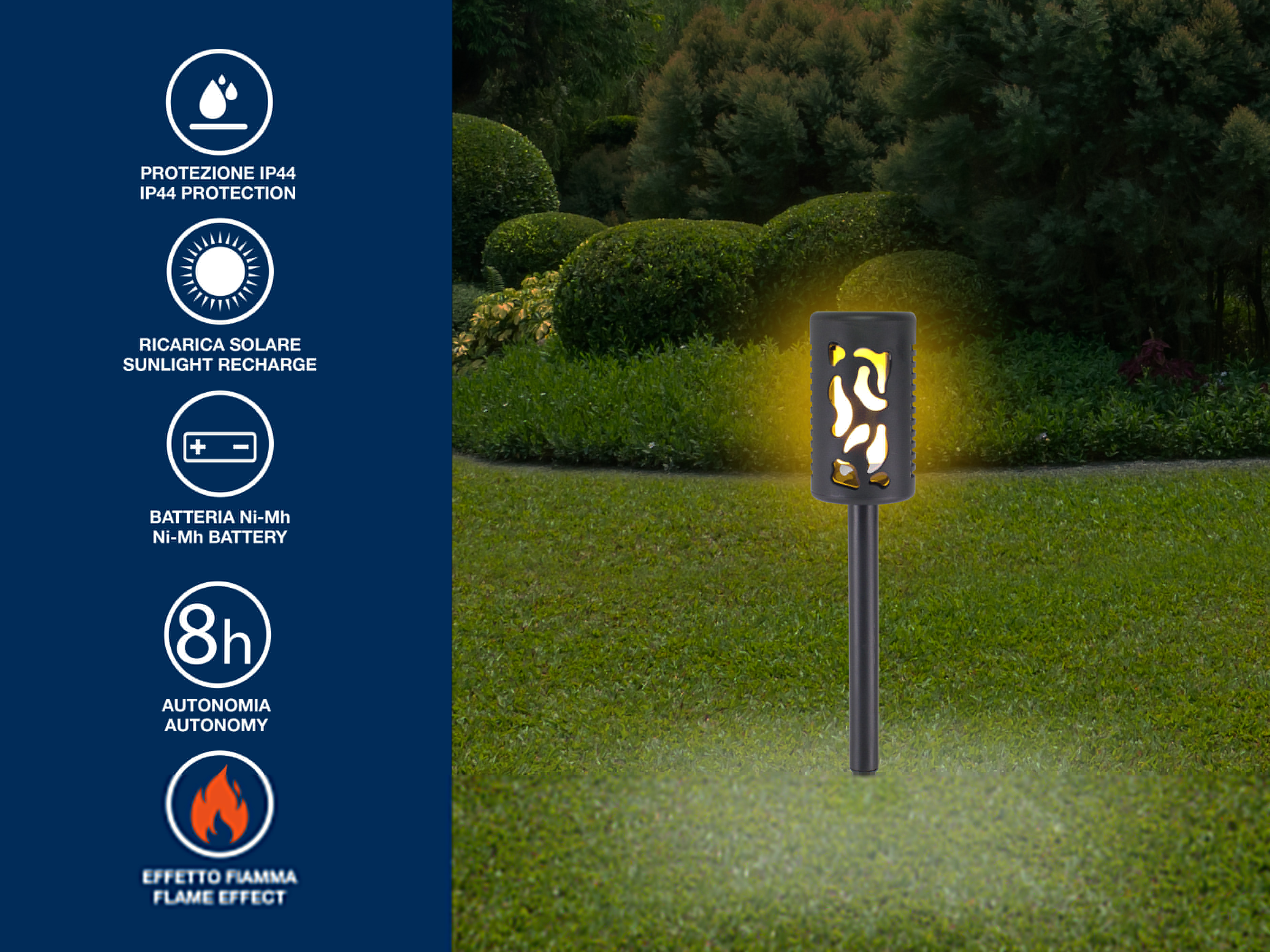 Una torcia solare da giardino con effetto fiamma, in piedi su un prato verde. Ci sono cespugli verdi sullo sfondo.