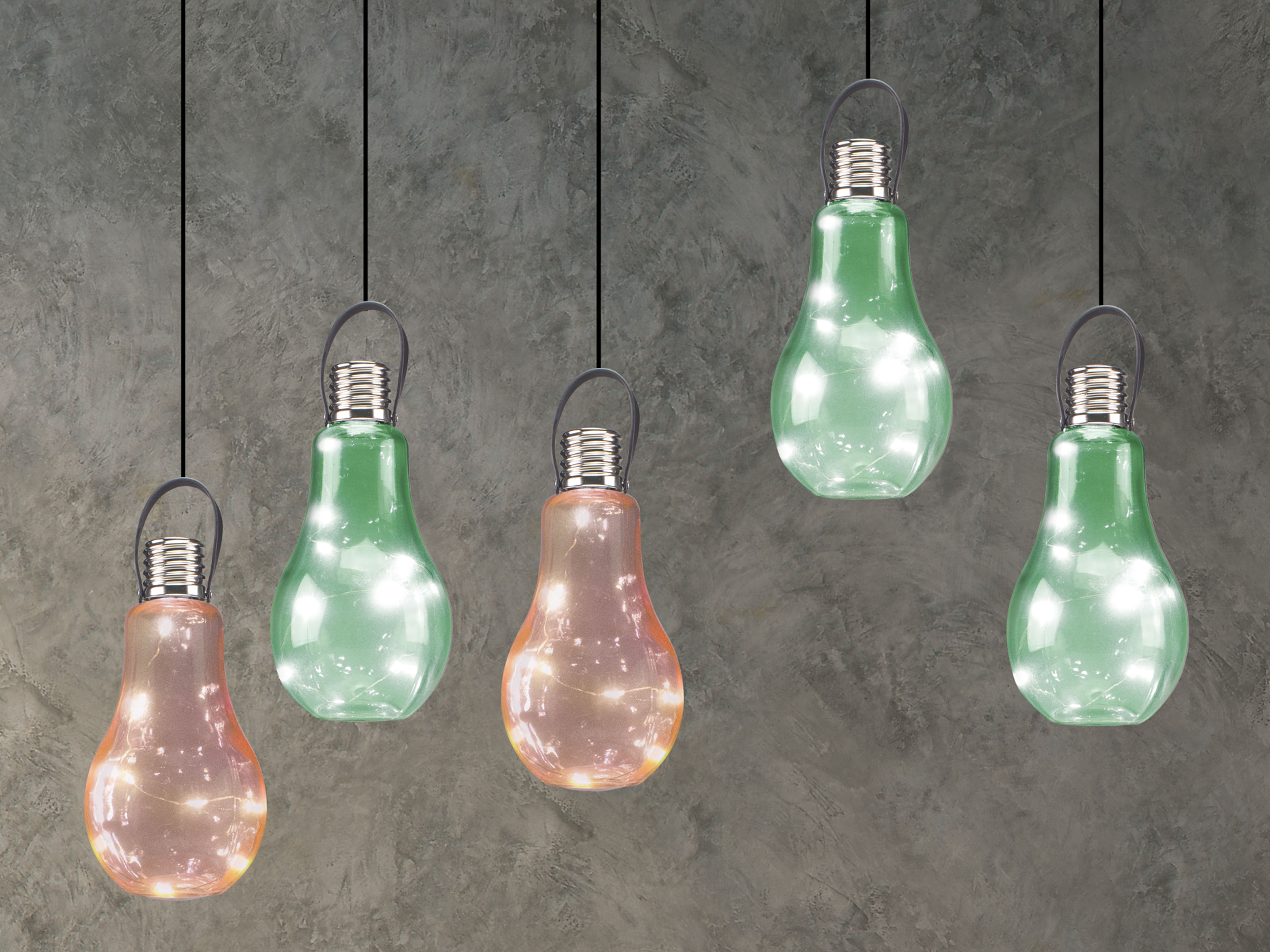 Cinque lampadine a sospensione con basi argentate e vetro di diversi colori. Lo sfondo è un muro grigio strutturato.