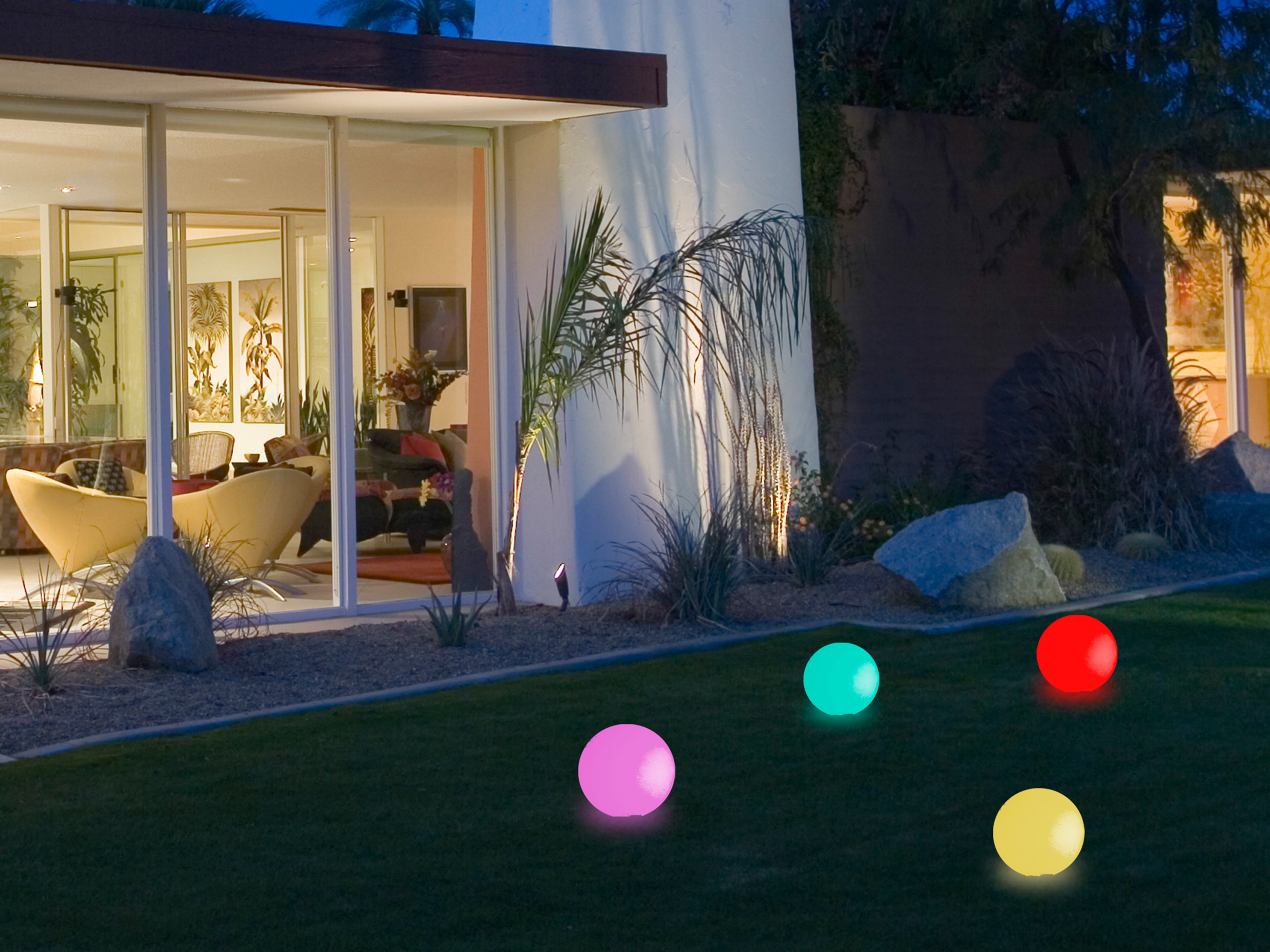 Una casa moderna con sfere illuminate sull'erba. La casa ha pareti di vetro. Le sfere sono rosa, blu, rosse e gialle.