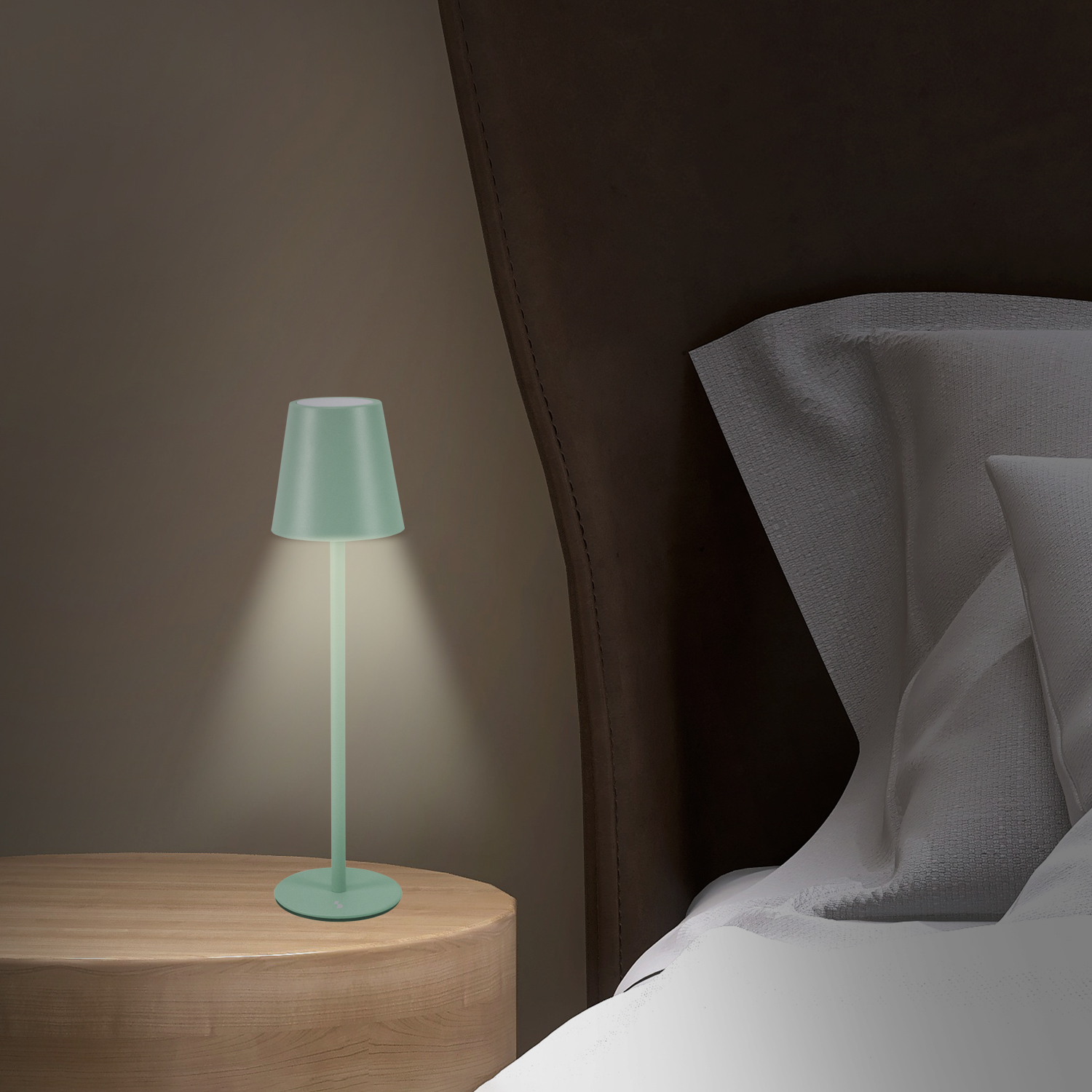 Una lampada verde menta su un tavolo di legno emette luce. Sullo sfondo un letto con lenzuola bianche e una testiera marrone.