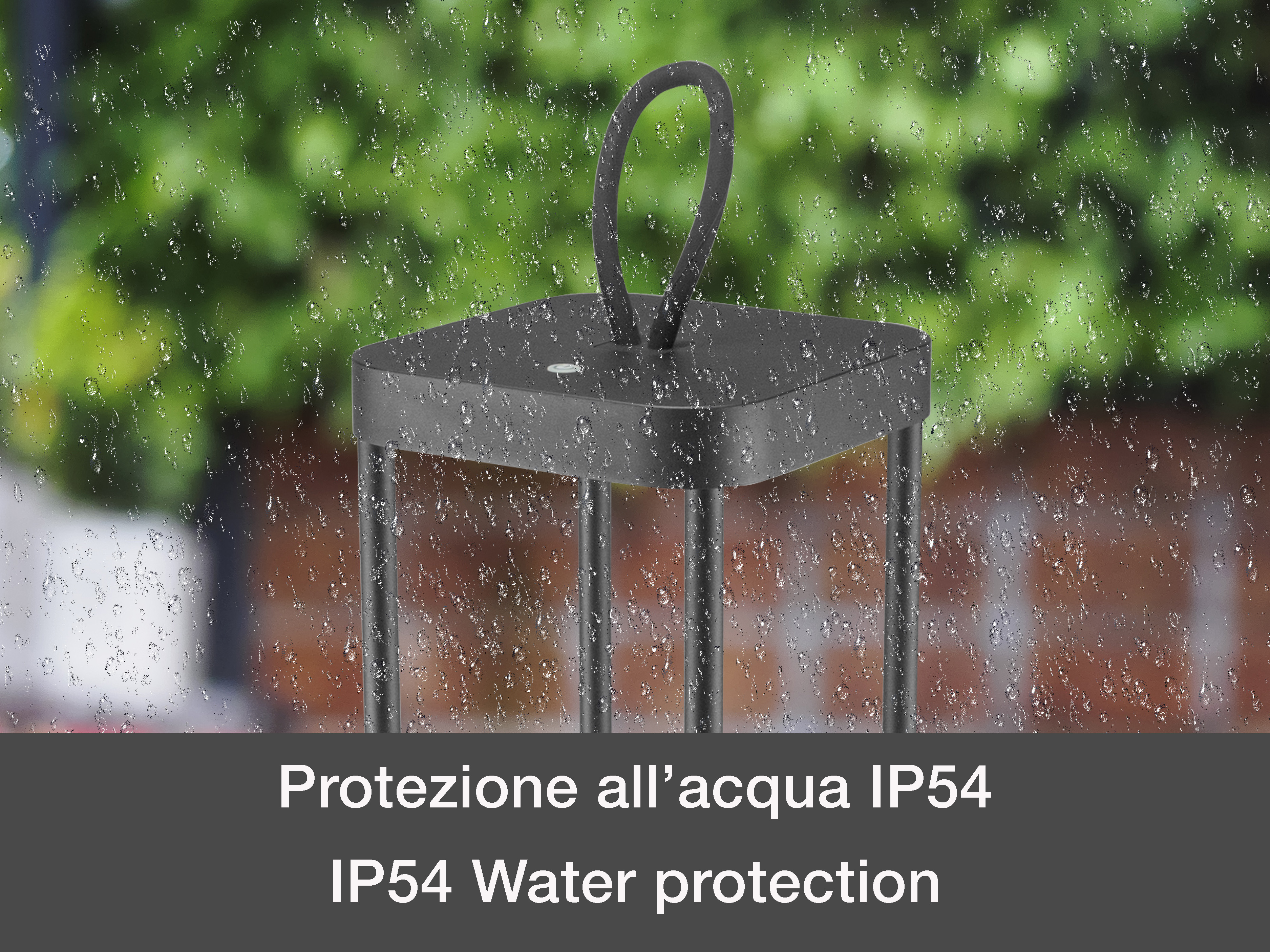 Una lampada nera con manico sotto la pioggia. Fogliame verde sullo sfondo. Gocce d'acqua visibili sulla lampada.