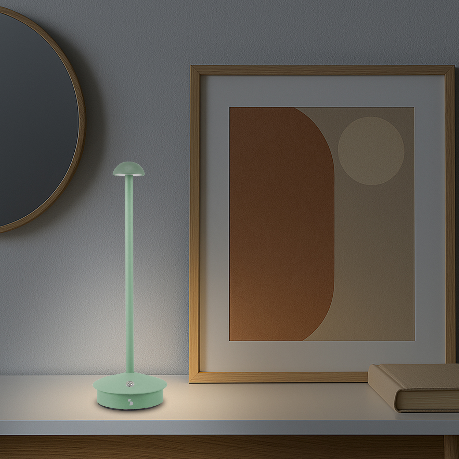Una lampada verde menta su una superficie bianca. Sullo sfondo un'opera d'arte incorniciata e uno specchio, con un libro.