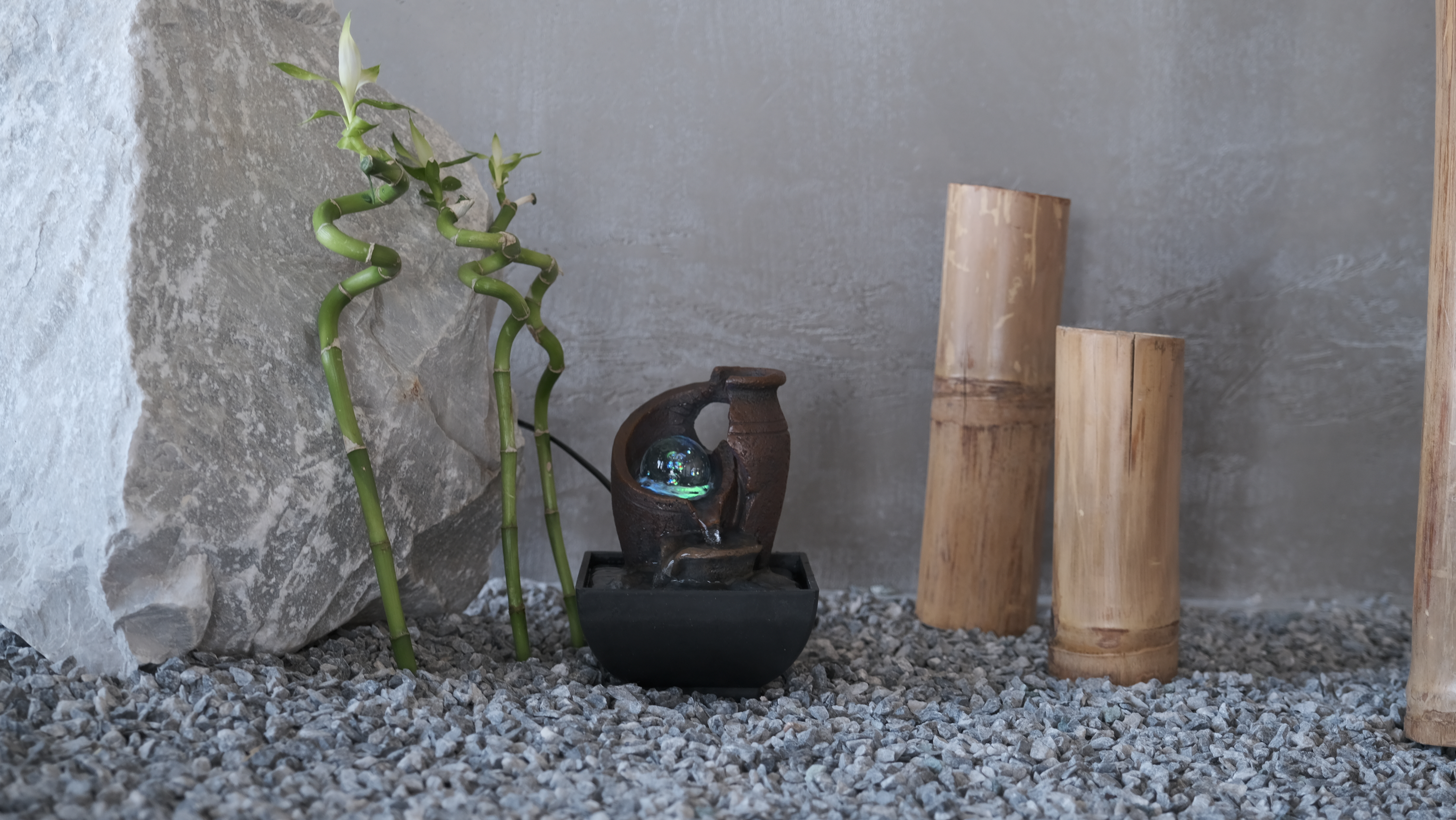 Una scena decorativa con una fontana, bambù e rocce. Una grande pietra è a sinistra. La fontana è al centro.