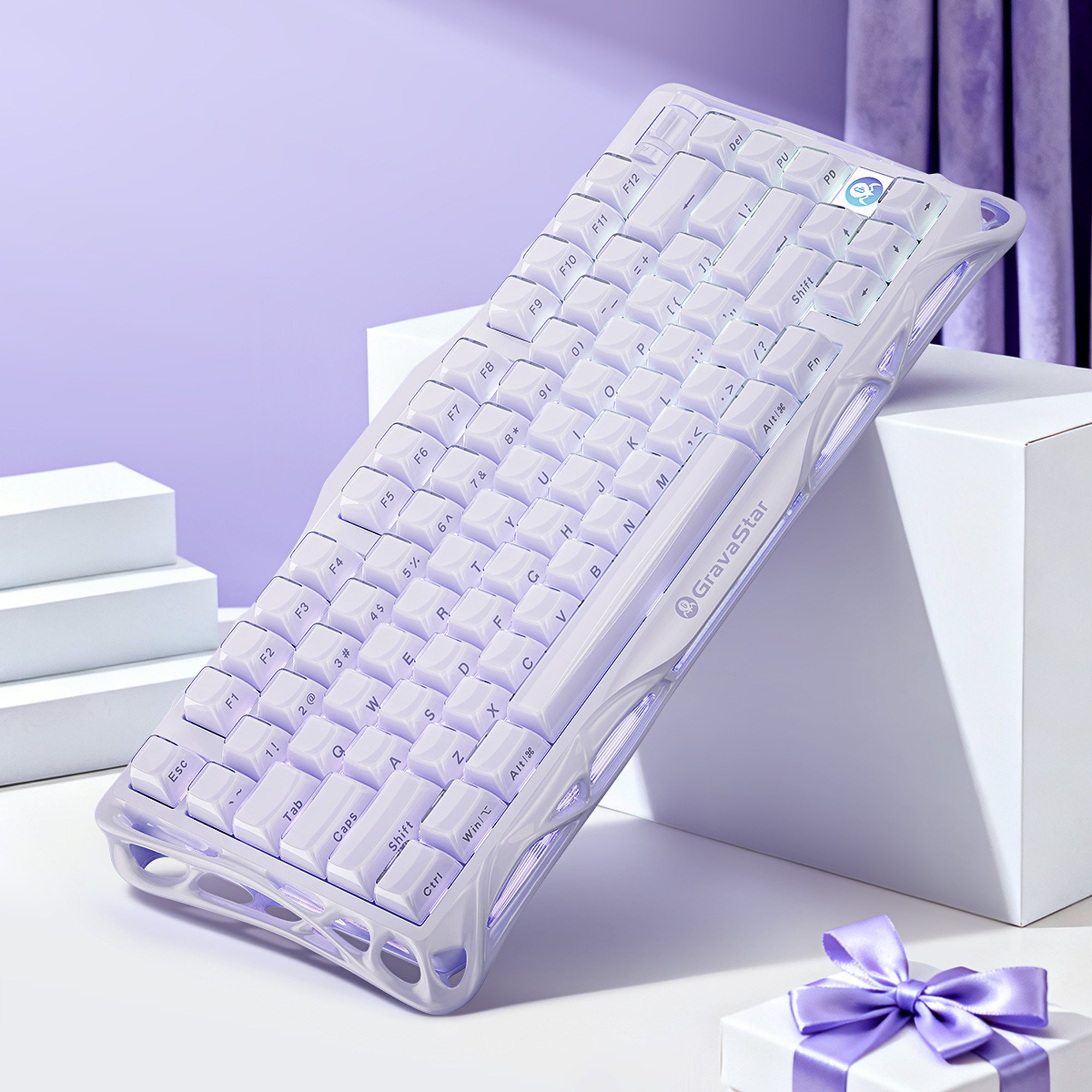 Biało-fioletowa klawiatura z podświetlanymi krawędziami jest ustawiona pod kątem na białej powierzchni z pudełkiem prezentowym i fioletową zasłoną.