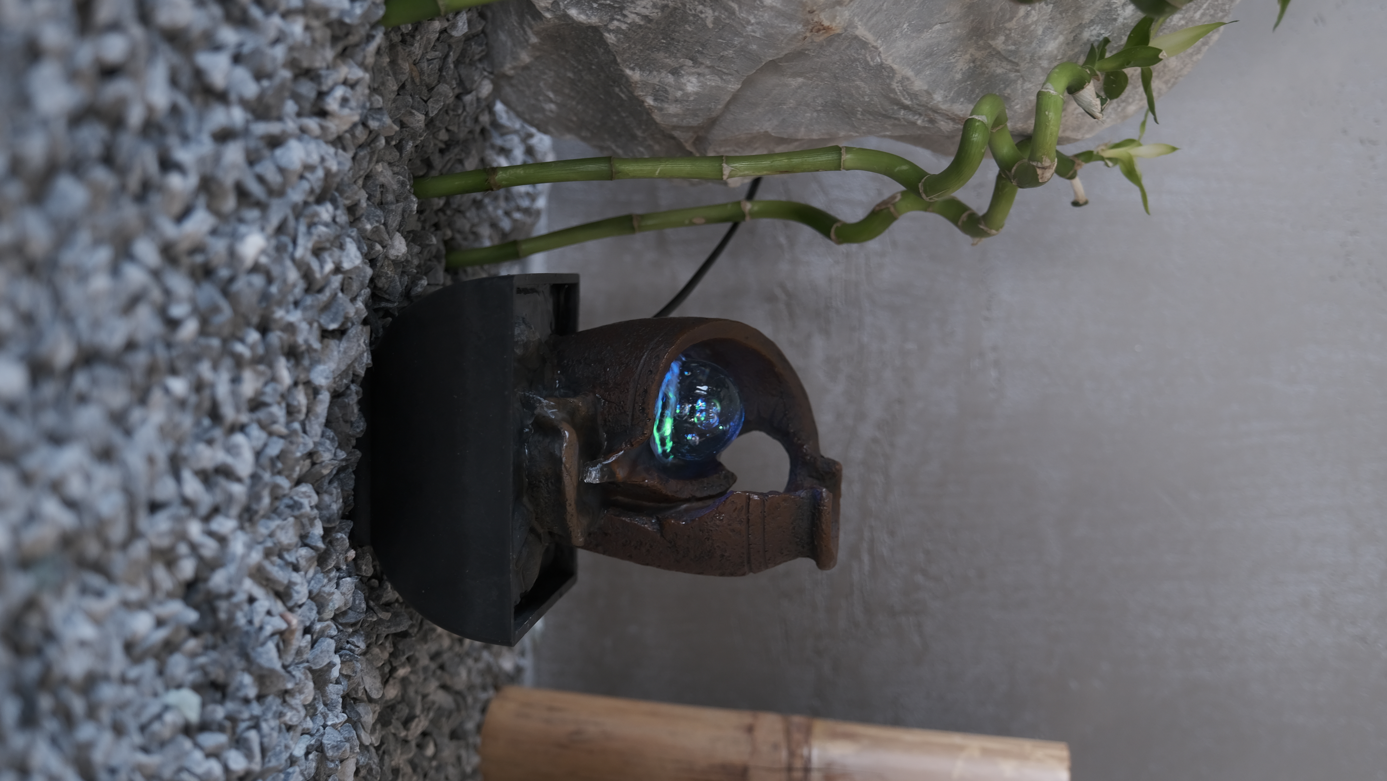Una piccola fontana con una palla di vetro all'interno. Steli di bambù verde e ghiaia sullo sfondo.