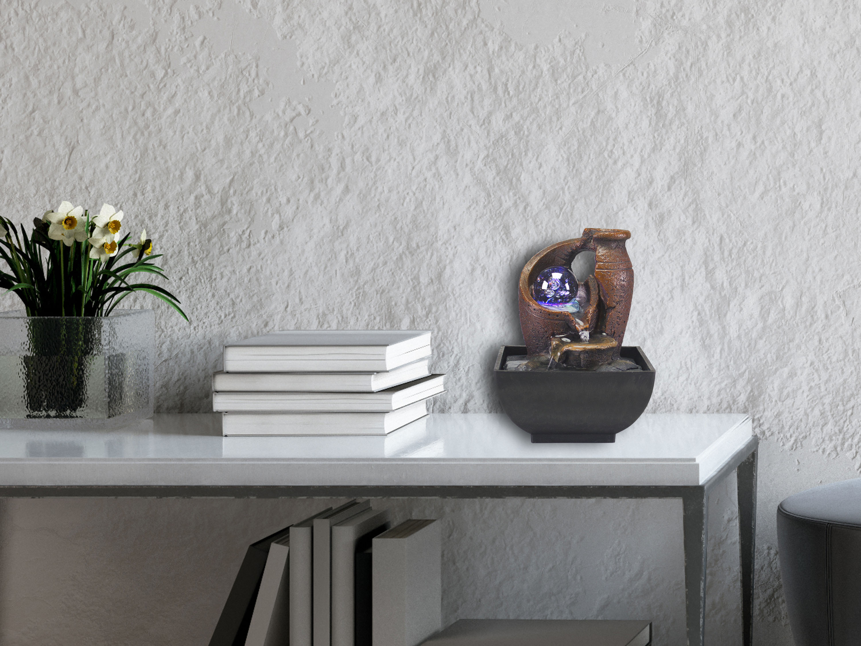 Una mensola decorativa con libri, una fontana d'acqua e fiori. Il muro è strutturato.