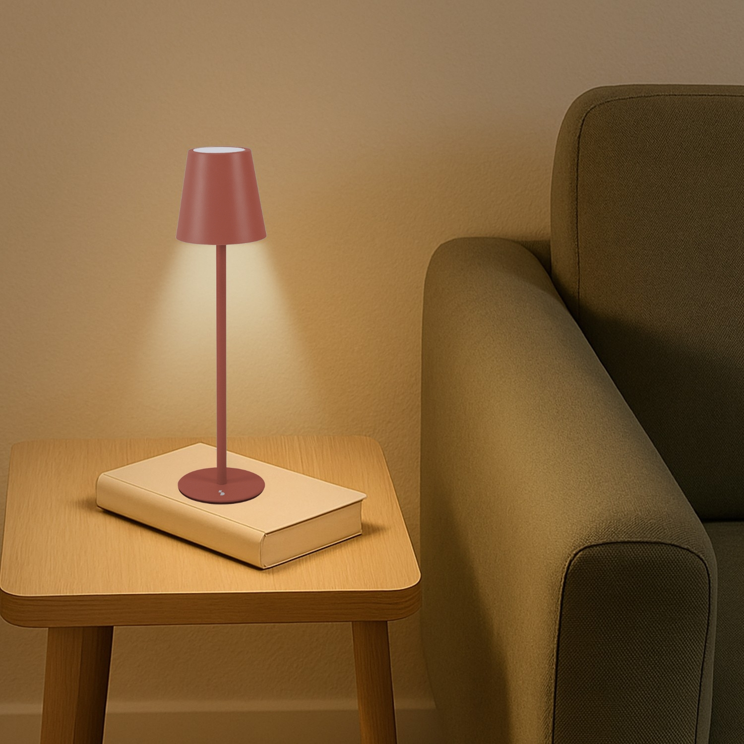 Una lampada amaranto su un libro su un tavolo di legno. Un divano verde a destra. Lo sfondo è una parete marrone chiaro.