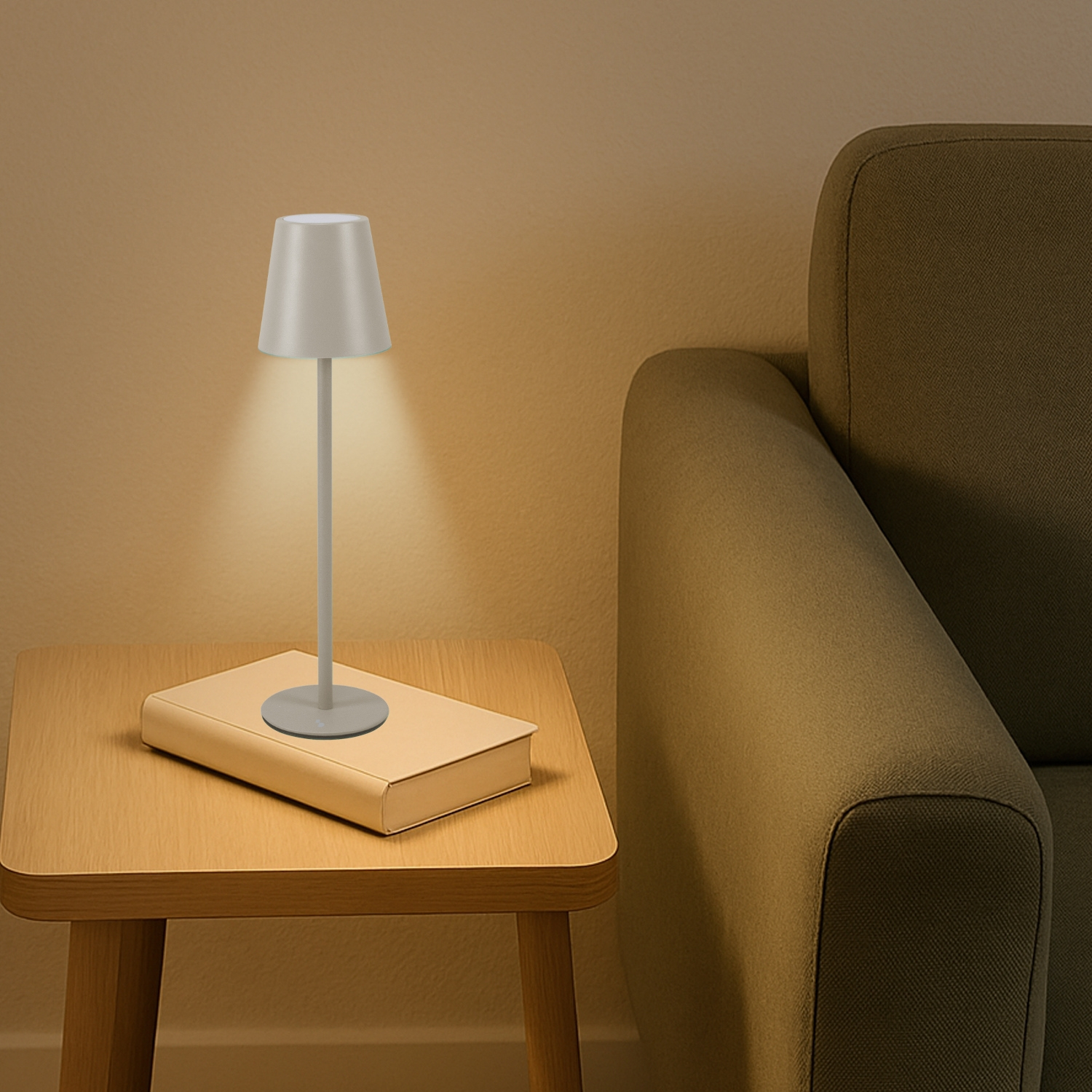 Una piccola lampada su un libro su un tavolo, con un divano sullo sfondo. La lampada è accesa, che proietta una luce calda.