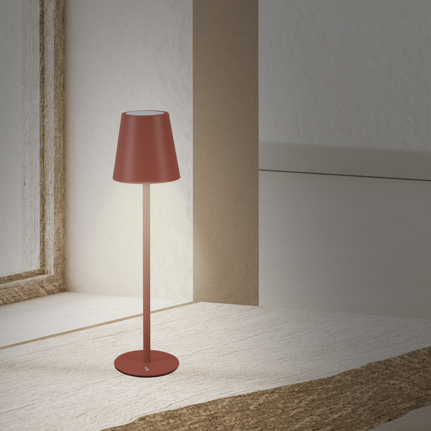 Una lampada rossa è su una superficie di legno chiaro. La lampada è accesa, emana un bagliore caldo. Lo sfondo è una parete bianca.
