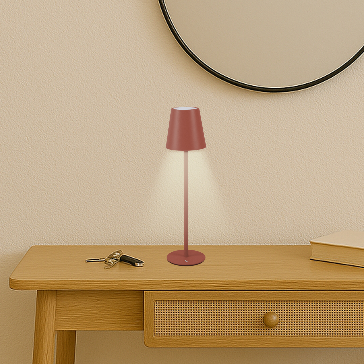 Una lampada bordeaux su un tavolo di legno, chiavi e un libro sono anche sul tavolo. Uno specchio è appeso sopra.