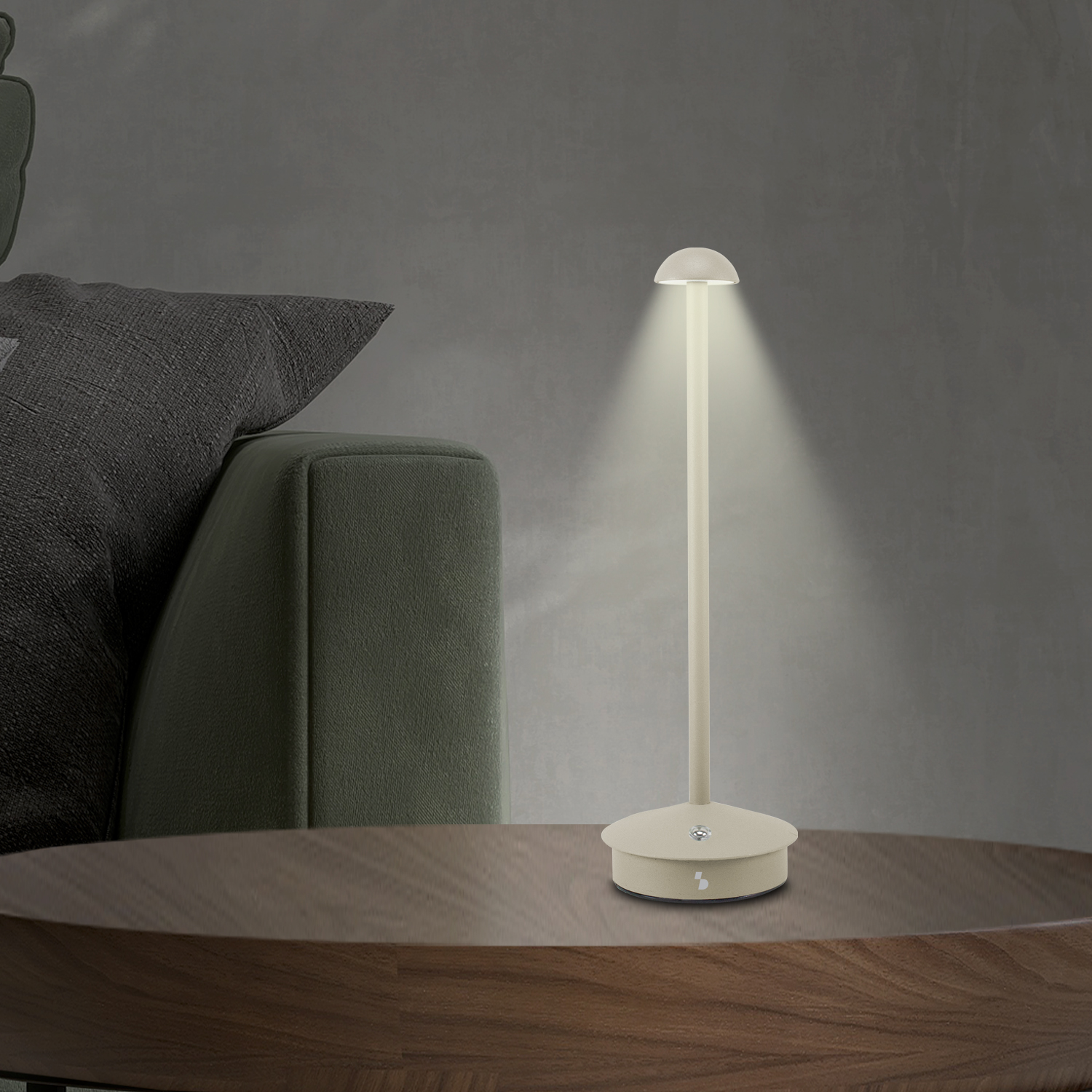 Una lampada beige su un tavolo di legno illumina l'area circostante. Sullo sfondo un divano verde e una parete scura.