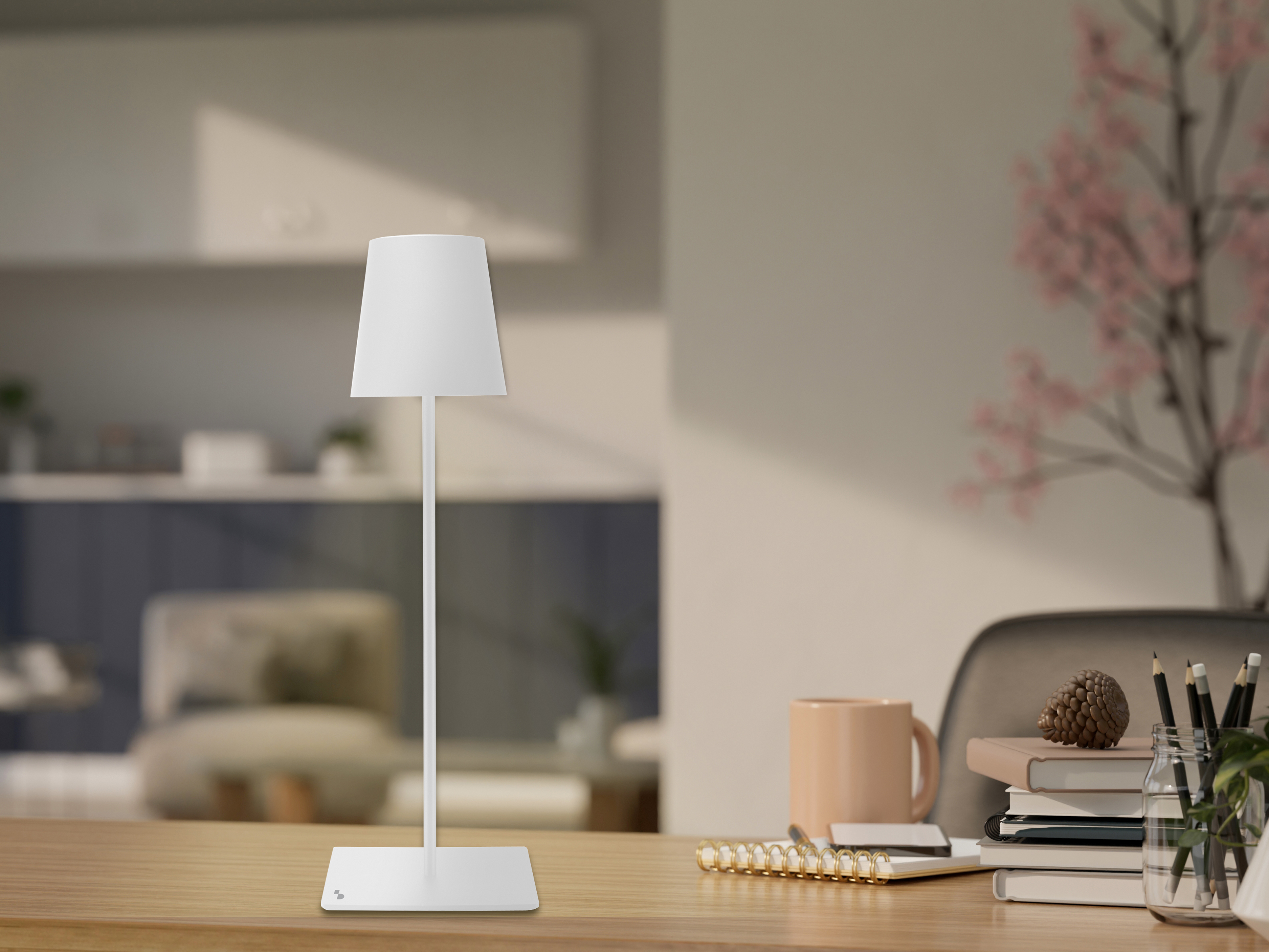 Una lampada bianca è su una scrivania in legno con una tazza, libri, matite e una pianta. Una pianta con fiori rosa è sullo sfondo.